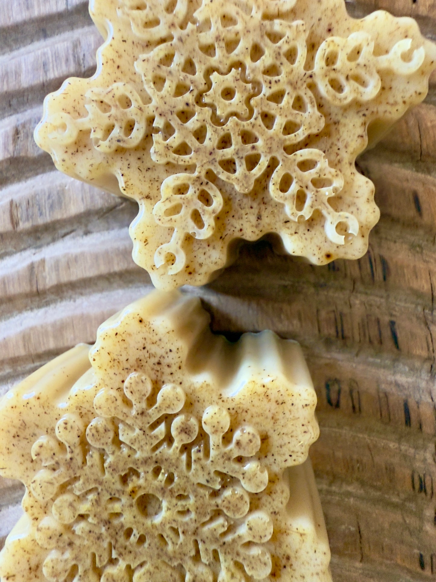 Golden goat milk snowflake soaps with natural licorice root speckling and detailed molded patterns on a wood board.