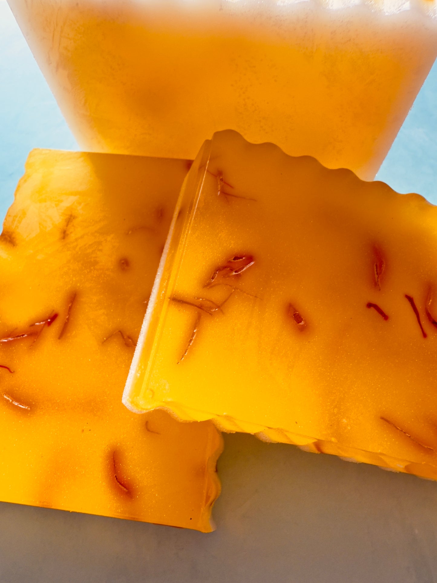 Golden yellow crinkle-cut soap bars with visible saffron threads, layered over a creamy white goat milk base, photographed on a soft gray background.