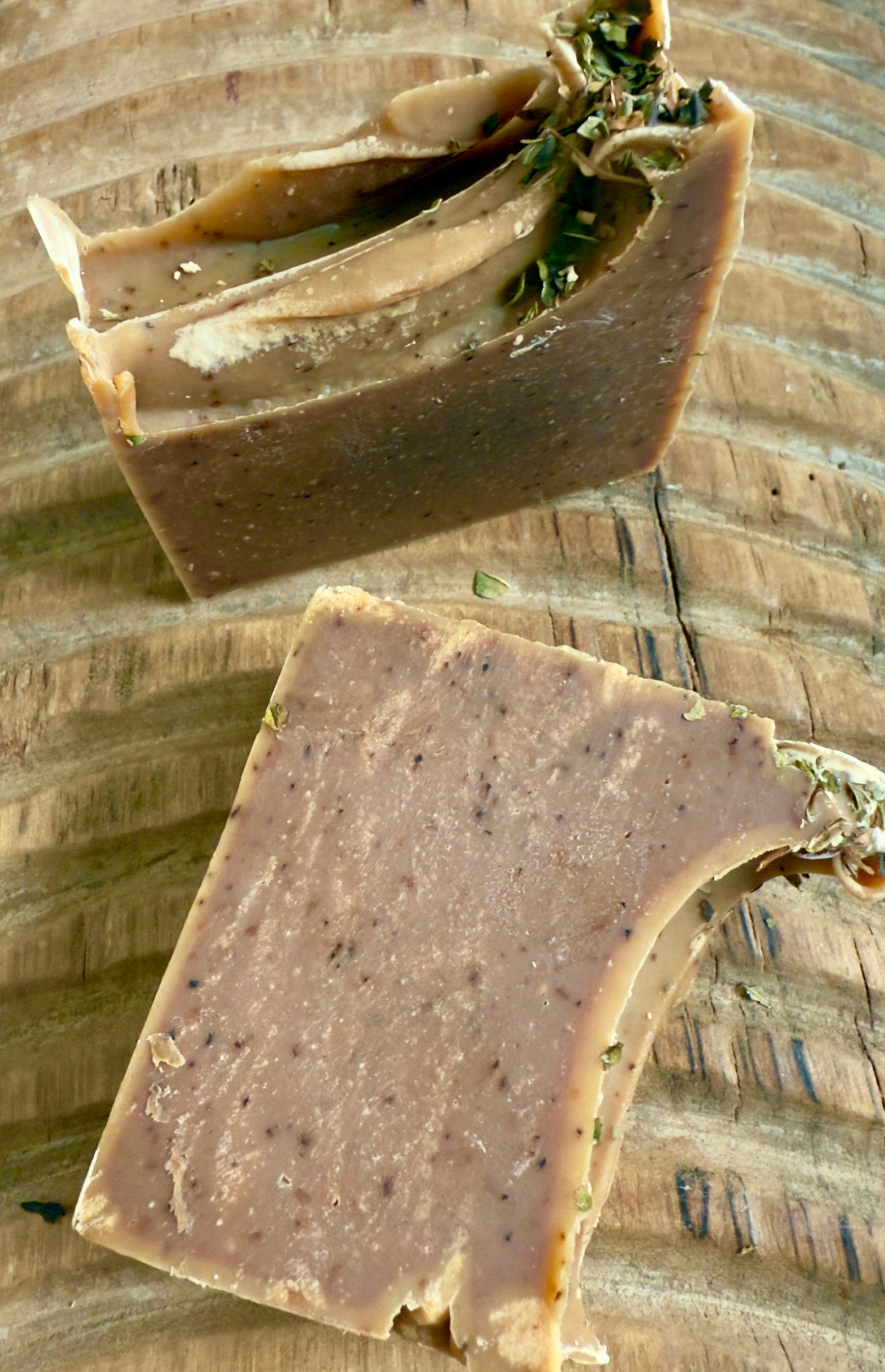 Deep brown Peppermint Cocoa cold process soap topped with crushed peppermint leaves on rustic wood.