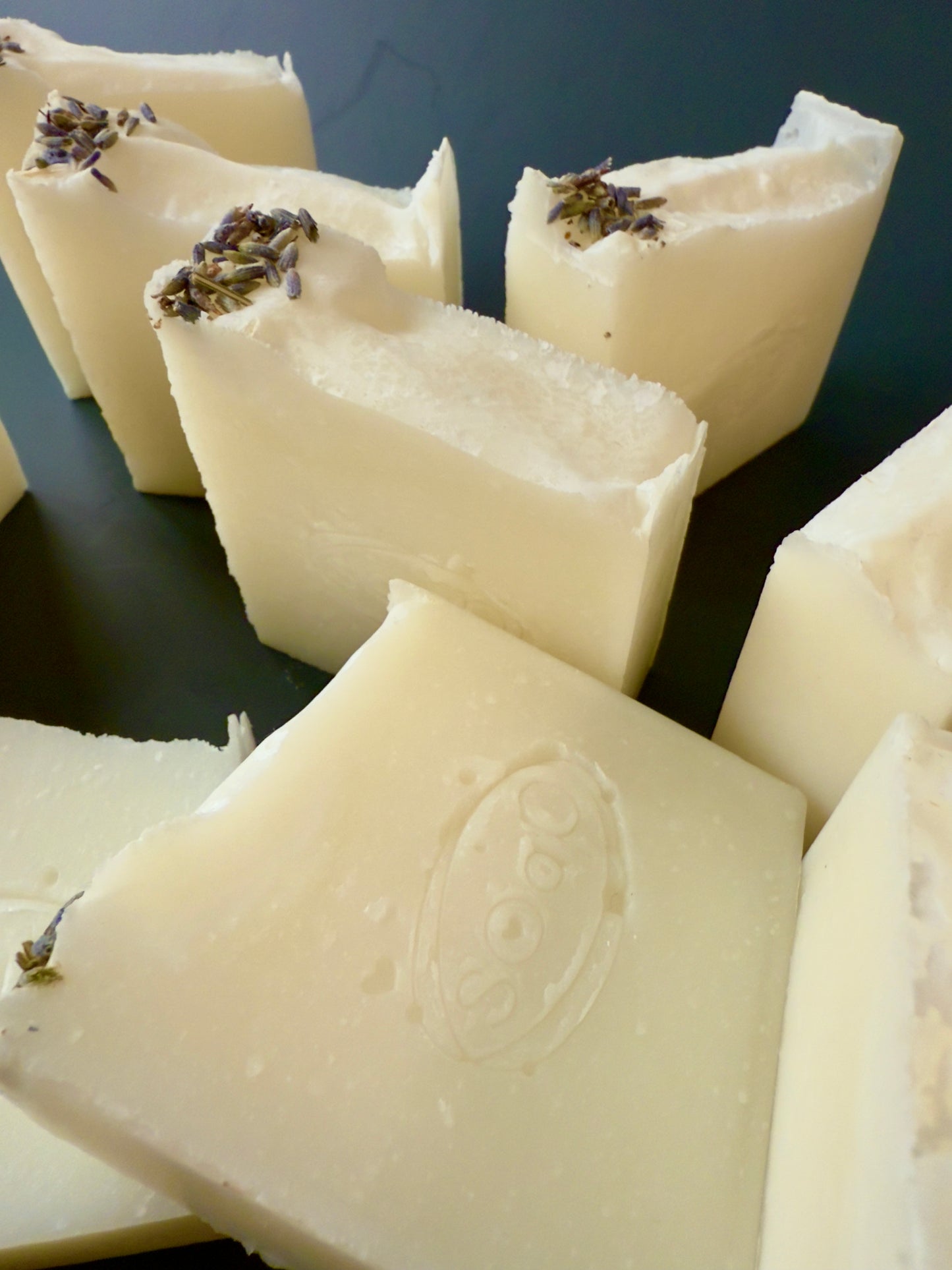 Creamy white tallow soap bars with lavender buds on top, arranged against a dark background.