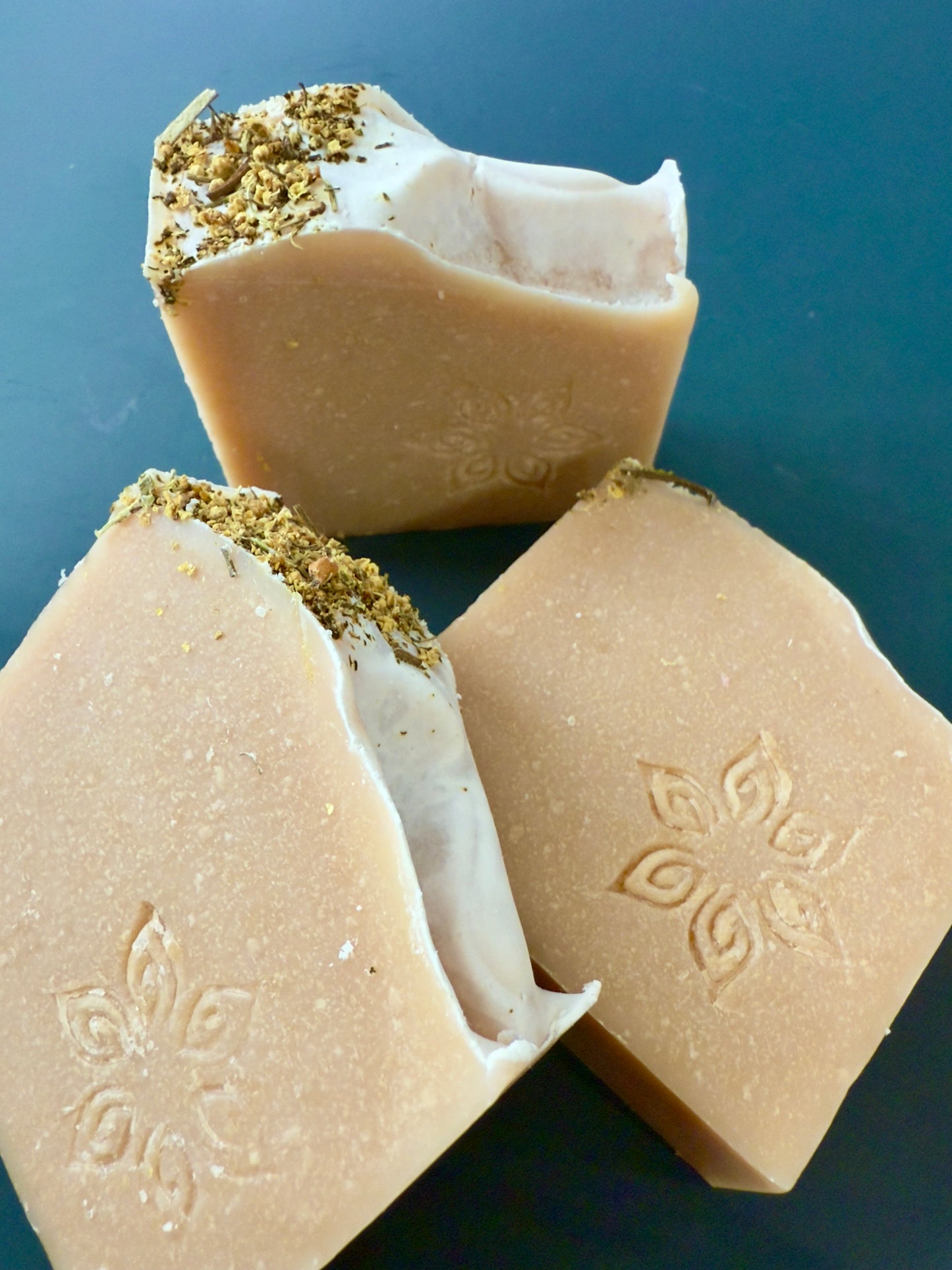 Close-up of a bar of soap with an embossed design on a blue background. Handcrafted pear-inspired soap with blush tones and elder flowers on top.