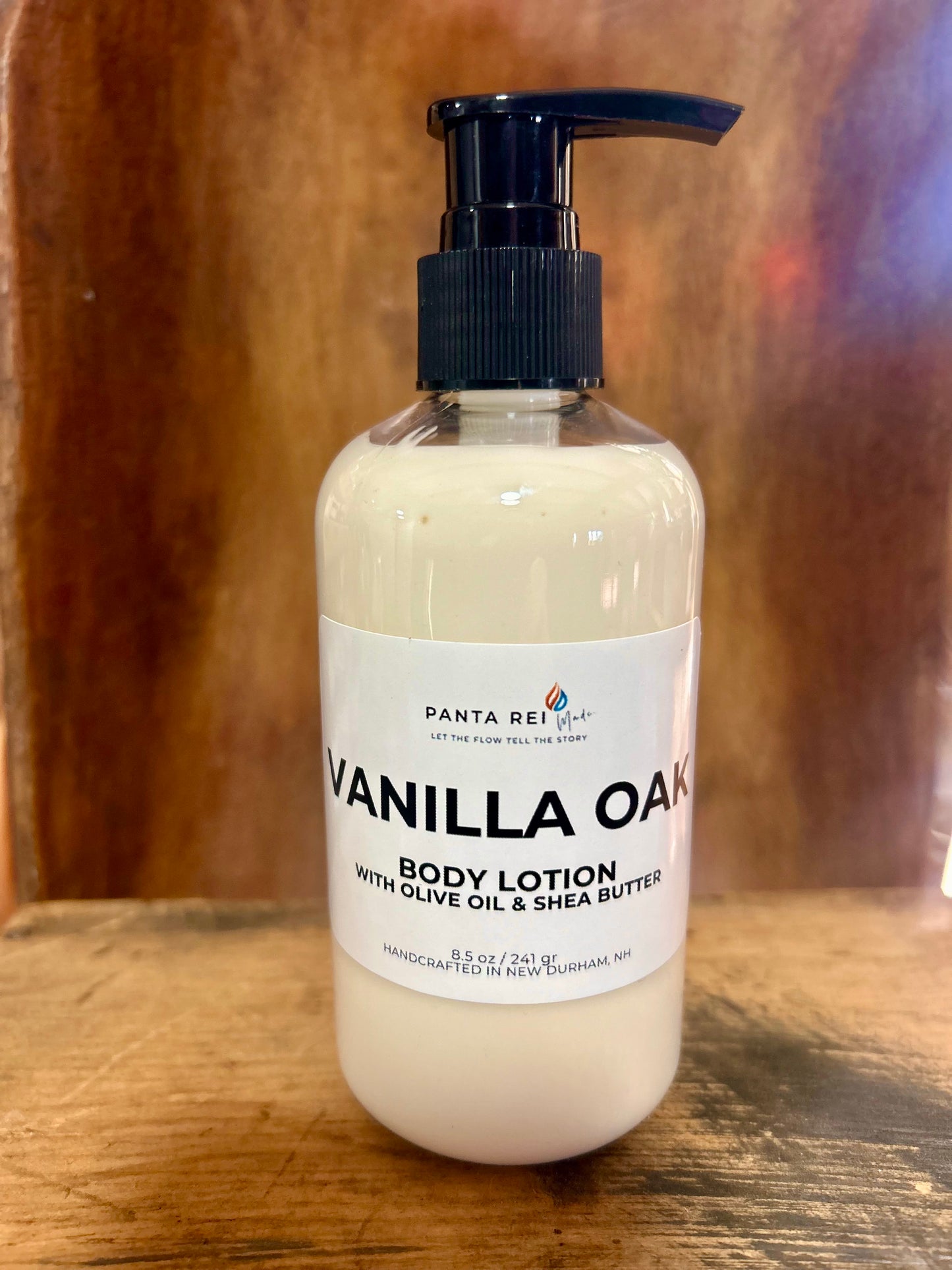 Vanilla Oak body lotion in a clear pump bottle with a minimalist label, photographed on a warm wood background.