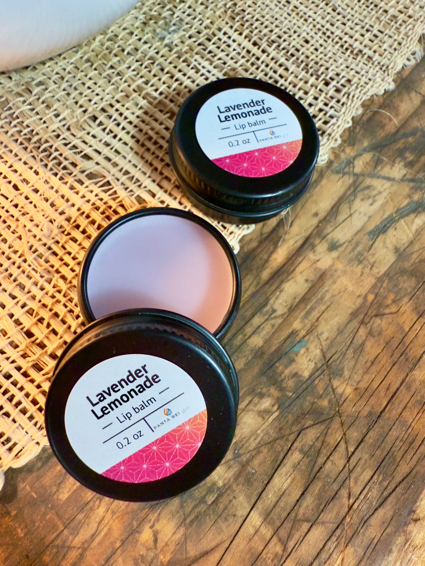 Lavender Lemonade lip balm in a black tin on a wooden surface. Open tin of Lavender Lemonade lip balm showing smooth balm surface.