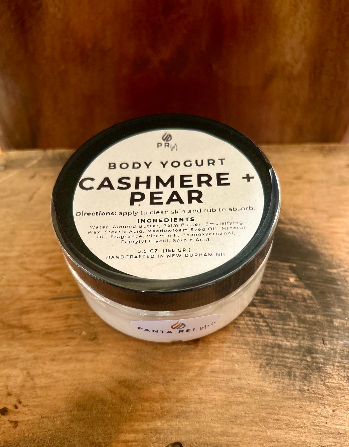 Jar of Cashmere + Pear Body Yogurt with black lid on a wooden surface, labeled Panta Rei Made.