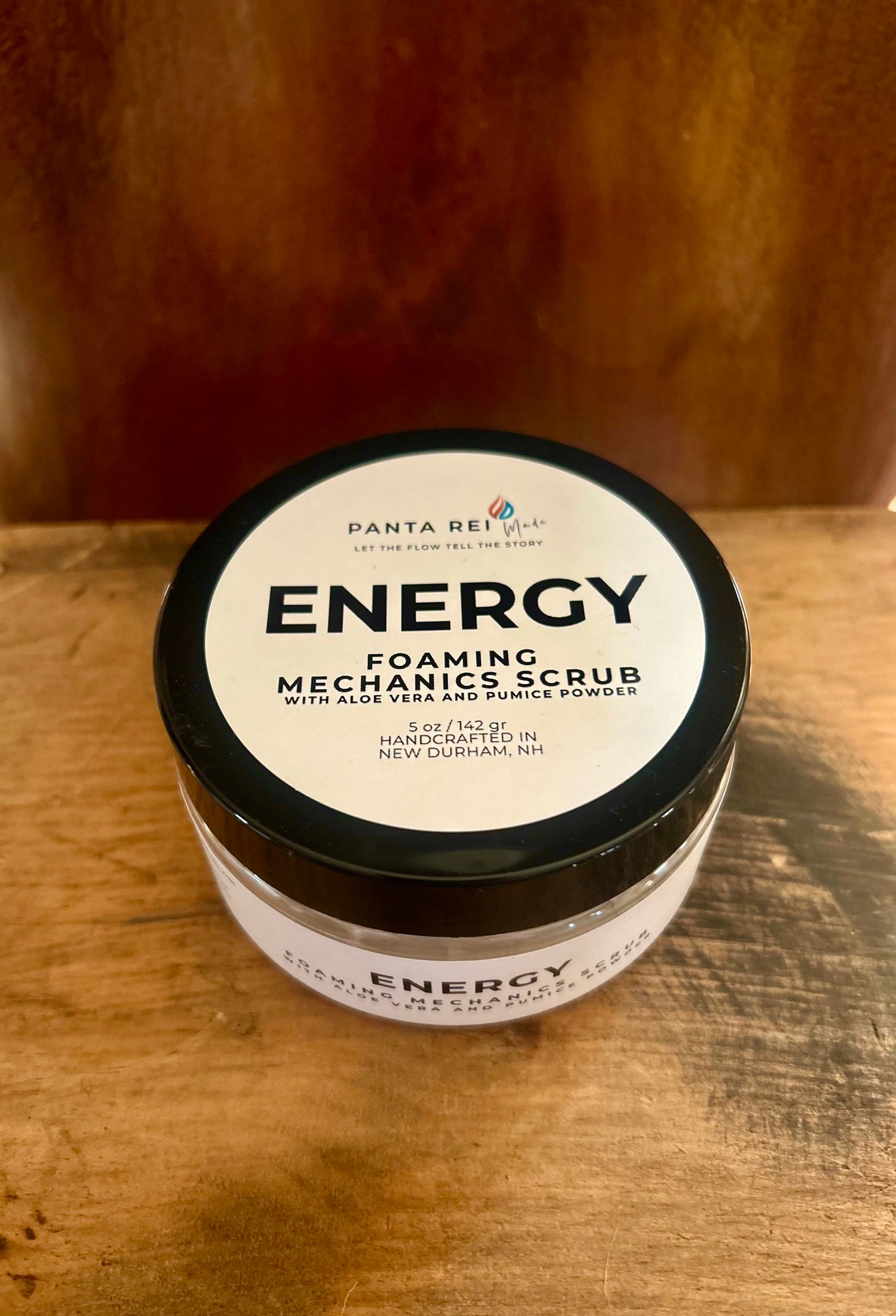 Energy foaming mechanic scrub in a black-lid jar with a minimalist label, photographed on a warm wood surface.