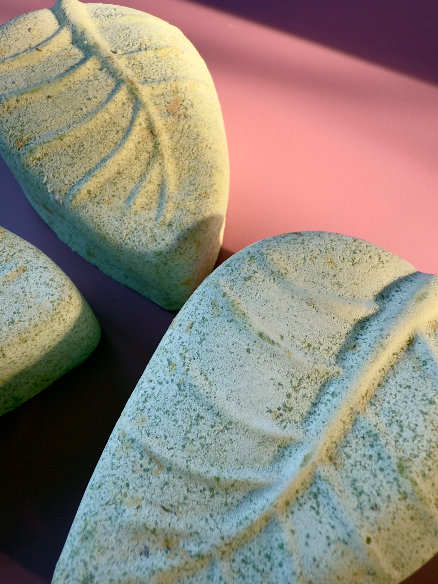 Two leaf-shaped soap bars with textured surfaces on a pink and purple gradient background