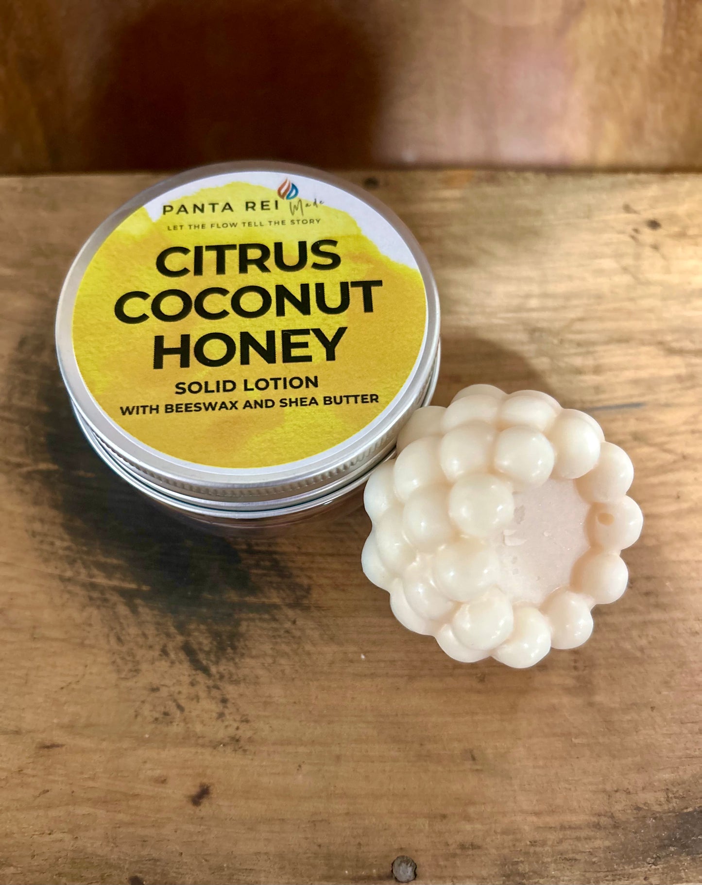 Solid lotion bar with a citrus-yellow tin labeled Citrus Coconut Honey, shown on a wooden surface.