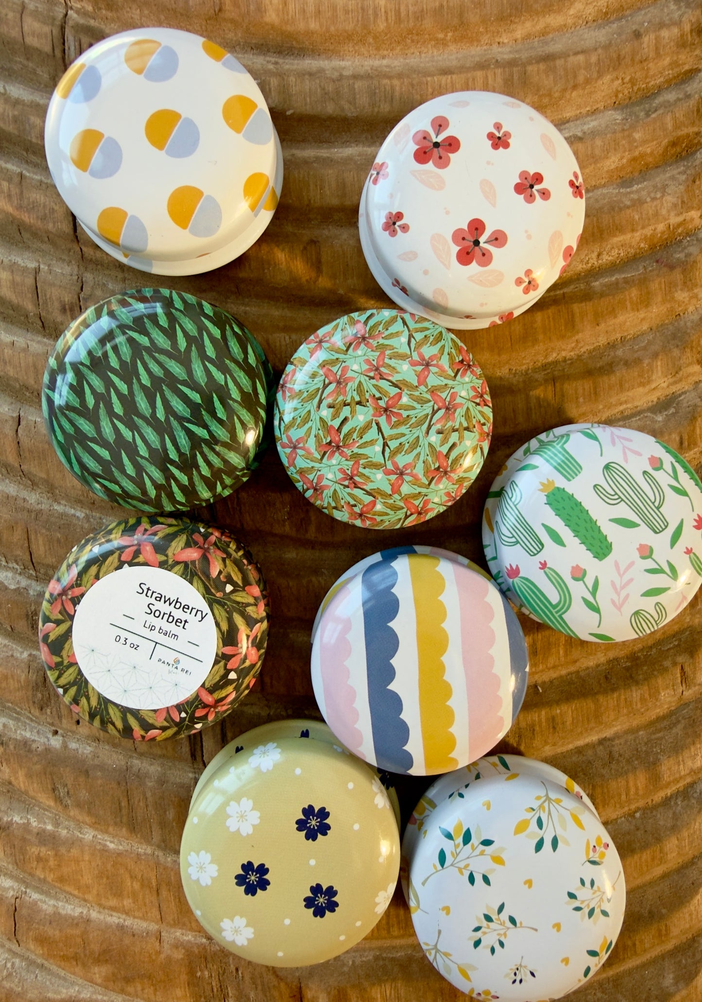 Strawberry Sorbet lip balm tin surrounded by colorful patterned tins on a carved wood surface.