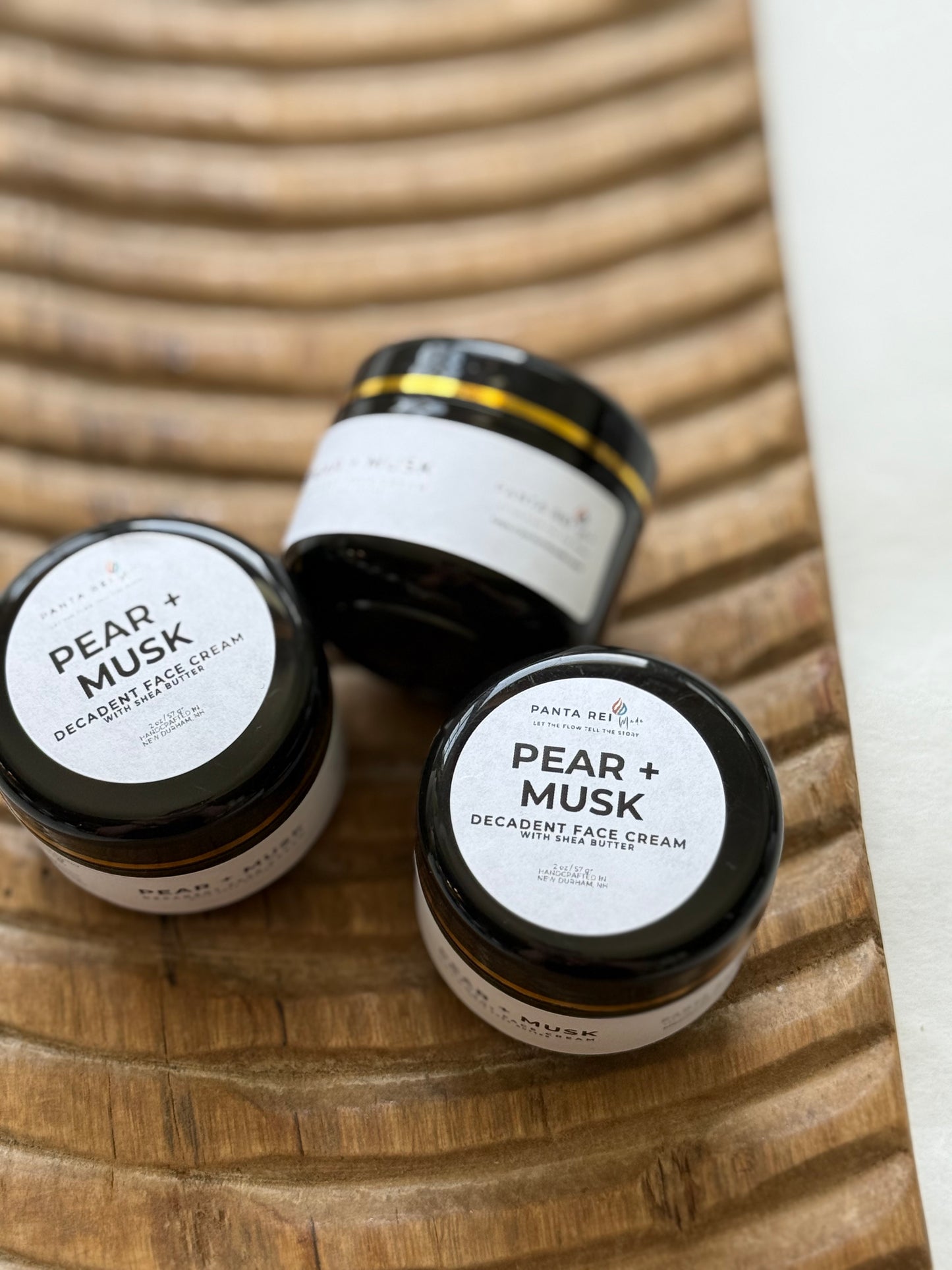 Three jars of Pear + Musk Decadent Face Cream on a wooden surface