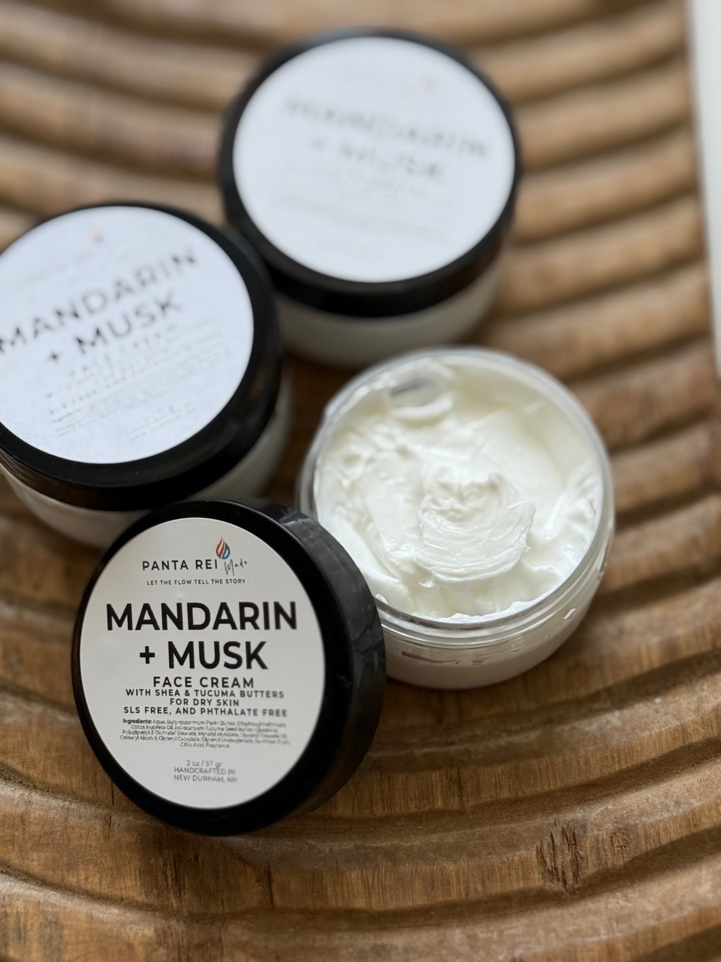 Three jars of Mandarin + Musk face cream on a wooden surface