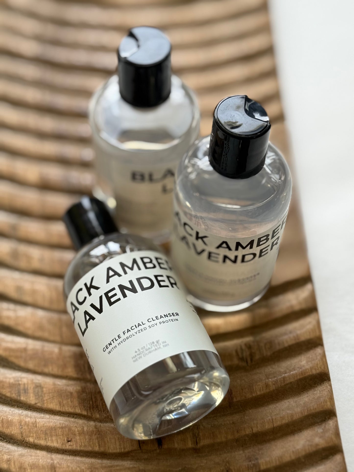 Three bottles of 'Black Amber Lavender' facial cleanser on a wooden surface