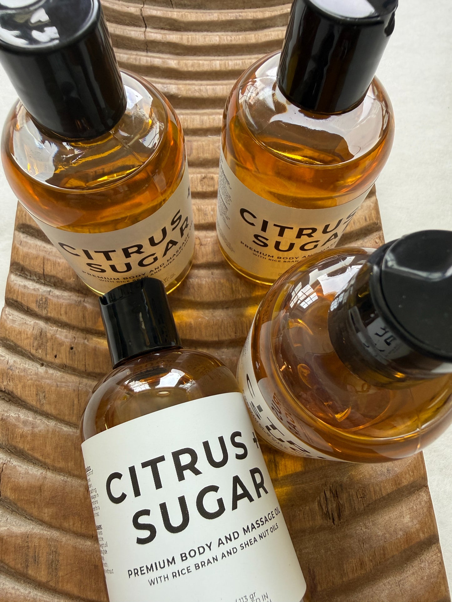 Four bottles of 'Citrus Sugar' massage oil on a wooden surface