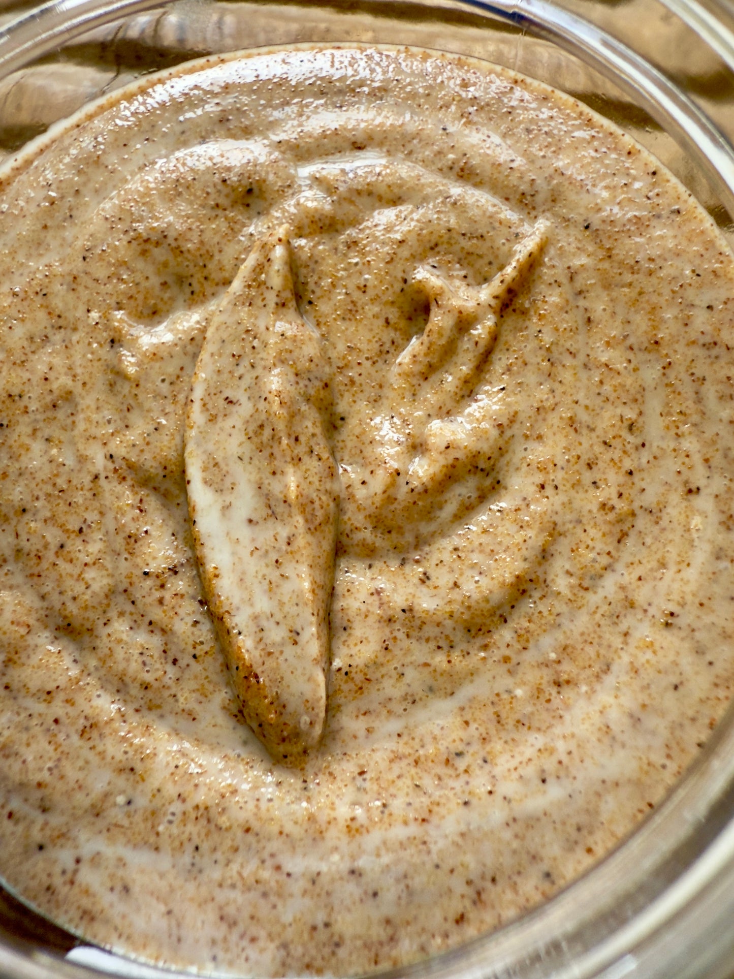 Close-up of creamy oat and honey scrub showing visible walnut shell exfoliating particles.