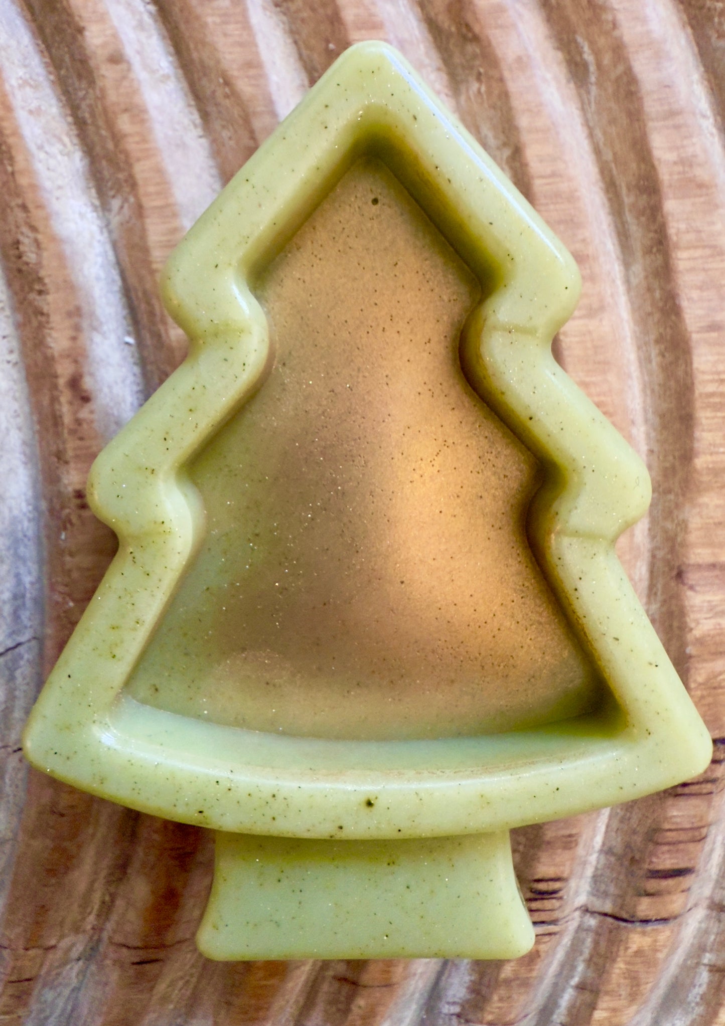 Green Christmas tree-shaped soap on a wooden surface. Green tree and snowflake holiday goat milk soaps with gold brushed tops and natural speckling.