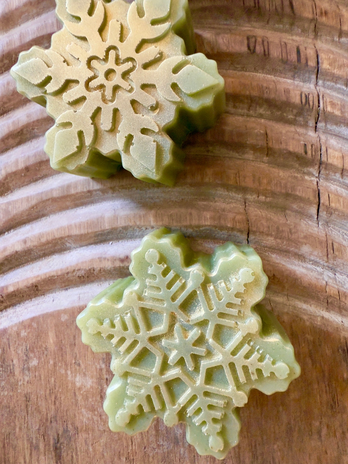 Green Christmas tree-shaped soap on a wooden surface. Green tree and snowflake holiday goat milk soaps with gold brushed tops and natural speckling.