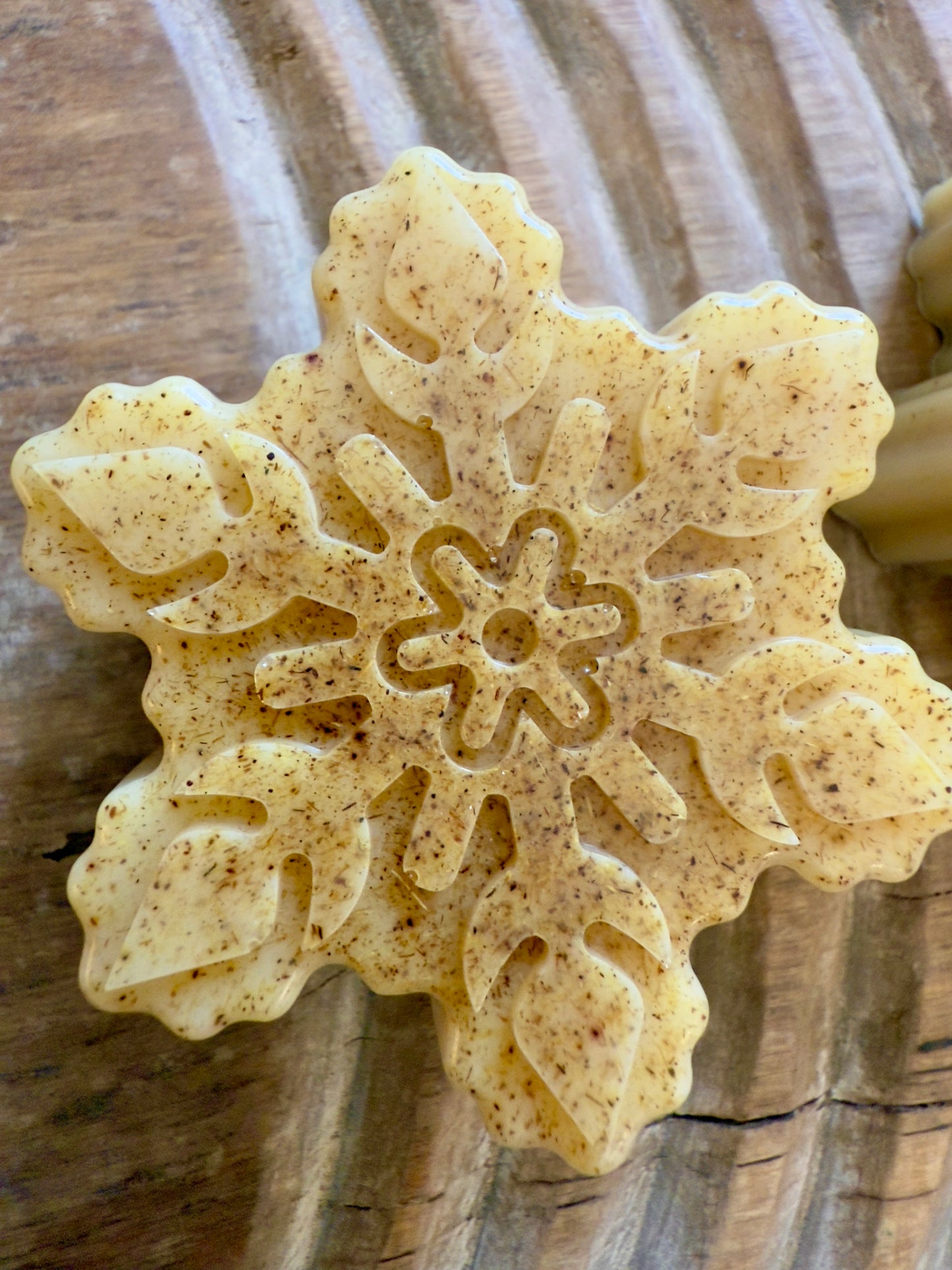 Golden goat milk snowflake soaps with natural licorice root speckling and detailed molded patterns on a wood board.