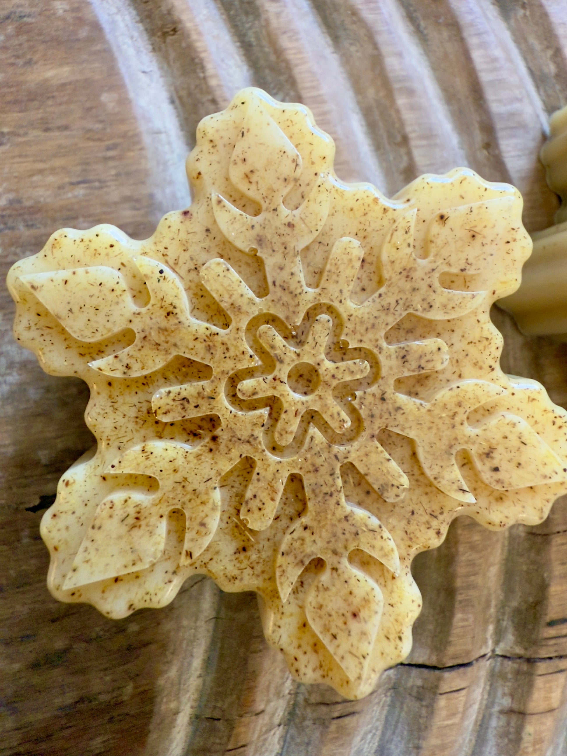 Golden goat milk snowflake soaps with natural licorice root speckling and detailed molded patterns on a wood board.