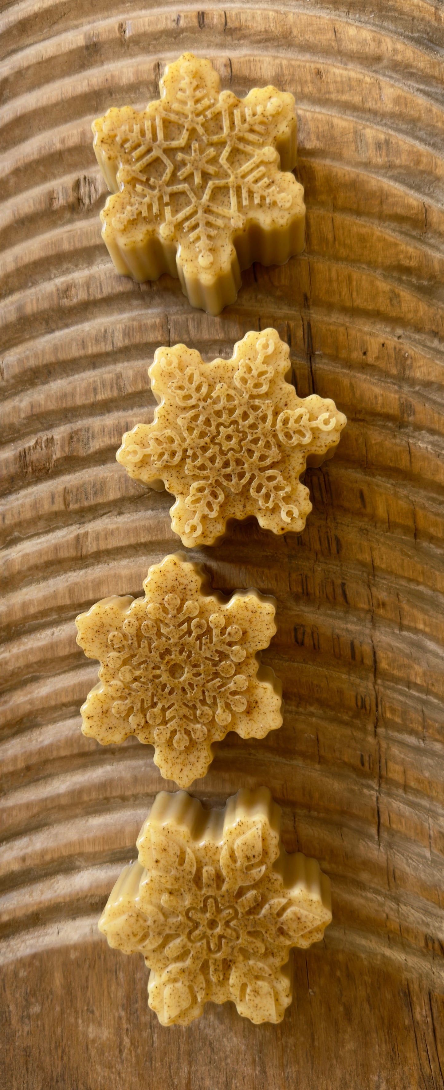 Golden goat milk snowflake soaps with natural licorice root speckling and detailed molded patterns on a wood board.