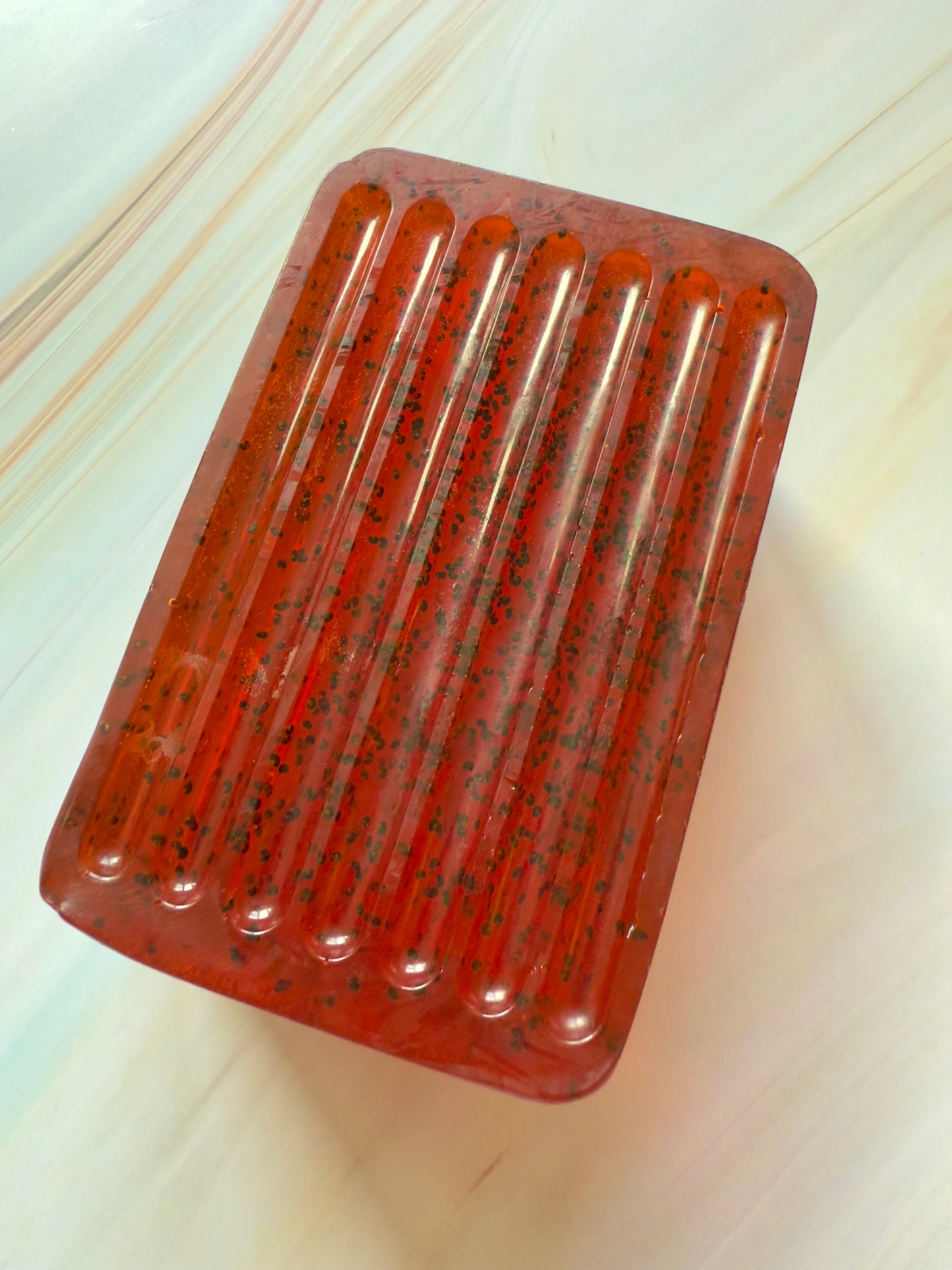Ruby red ridged soap bar with visible dark grape specks, photographed on a soft, marbled cream background.