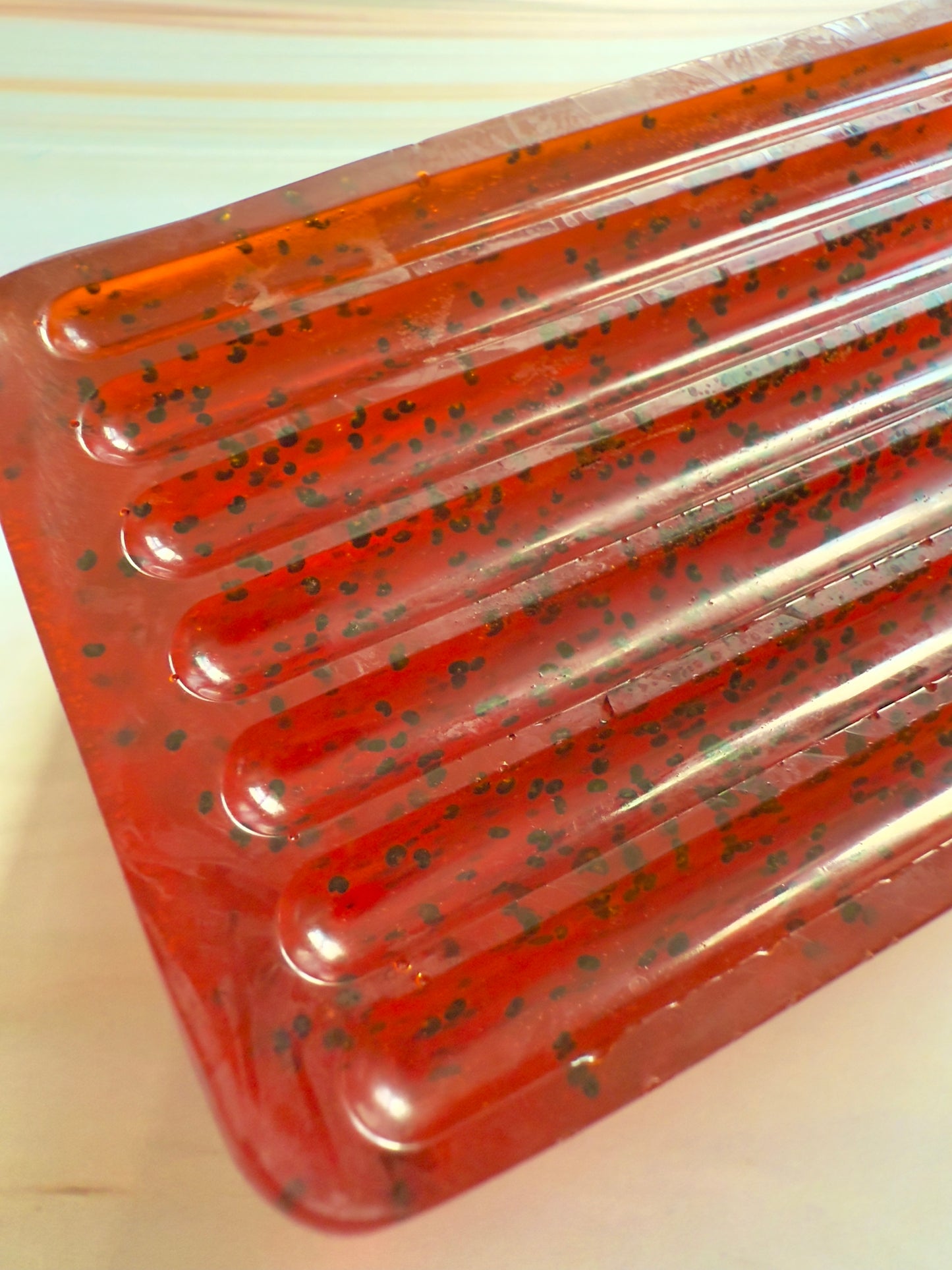 Ruby red ridged soap bar with visible dark grape specks, photographed on a soft, marbled cream background.