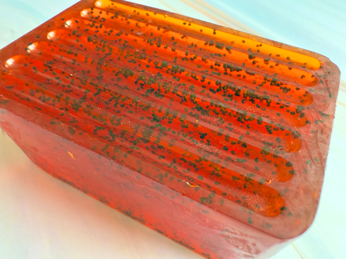 Ruby red ridged soap bar with visible dark grape specks, photographed on a soft, marbled cream background.