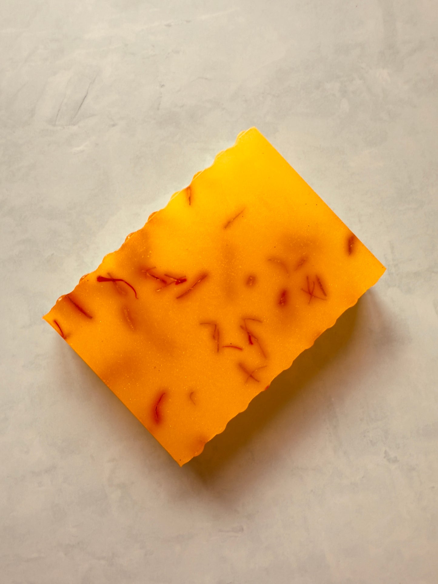 Golden yellow crinkle-cut soap bars with visible saffron threads, layered over a creamy white goat milk base, photographed on a soft gray background.
