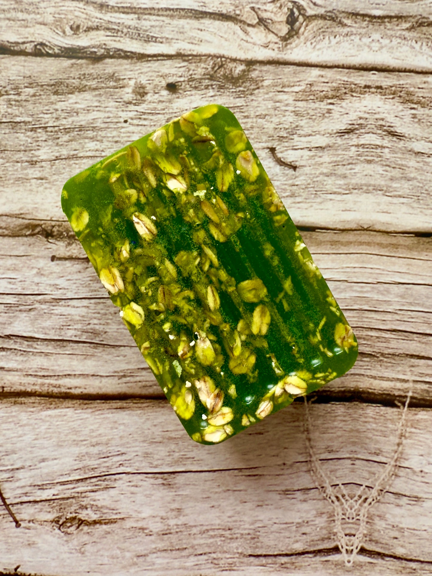 Translucent green glycerin soap bar with suspended oats on a wood background.