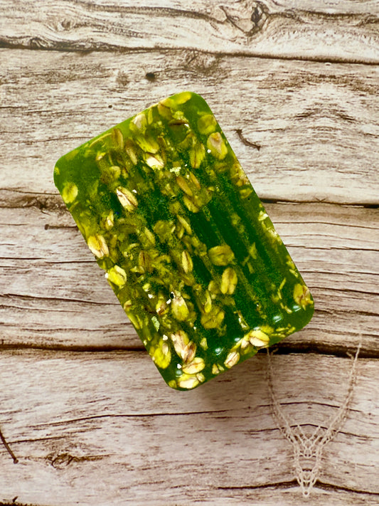 Translucent green glycerin soap bar with suspended oats on a wood background.