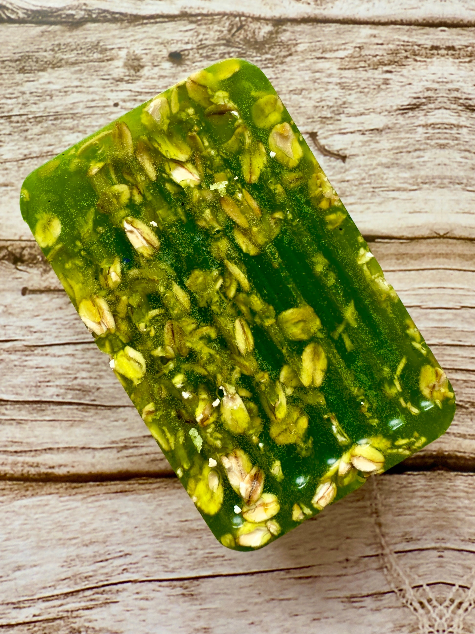Translucent green glycerin soap bar with suspended oats on a wood background.