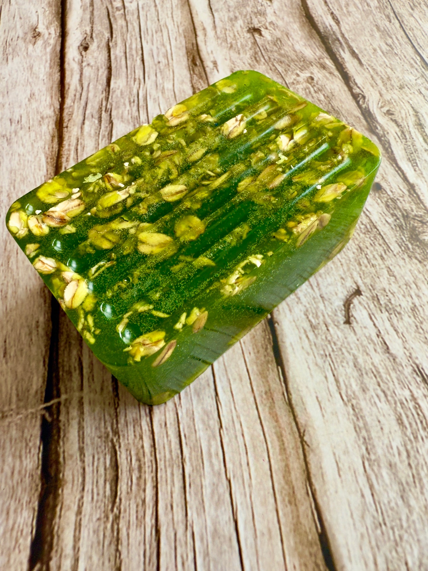 Translucent green glycerin soap bar with suspended oats on a wood background.