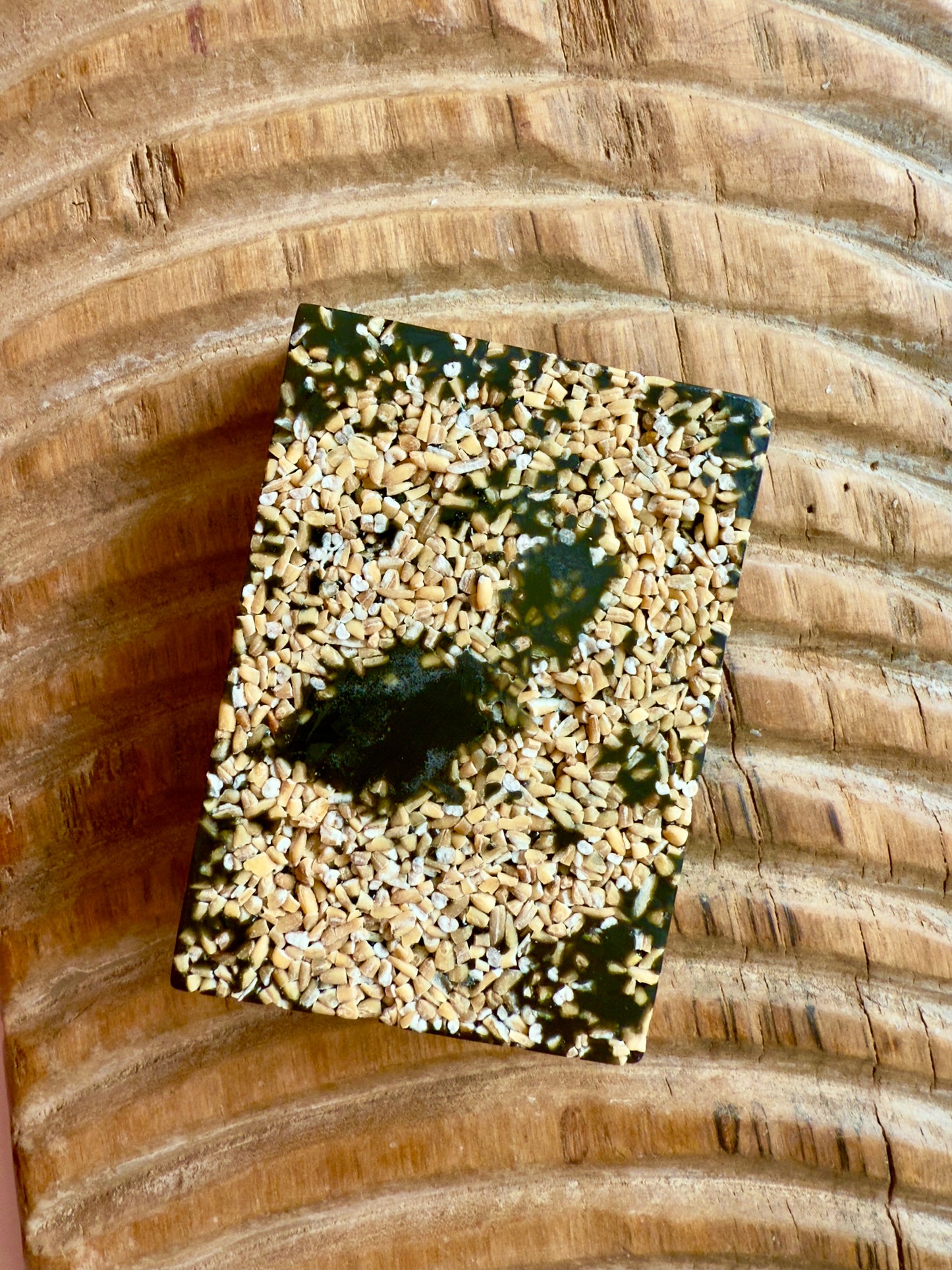 Dark African black soap bar topped with chopped oats, showing natural texture and rugged finish.