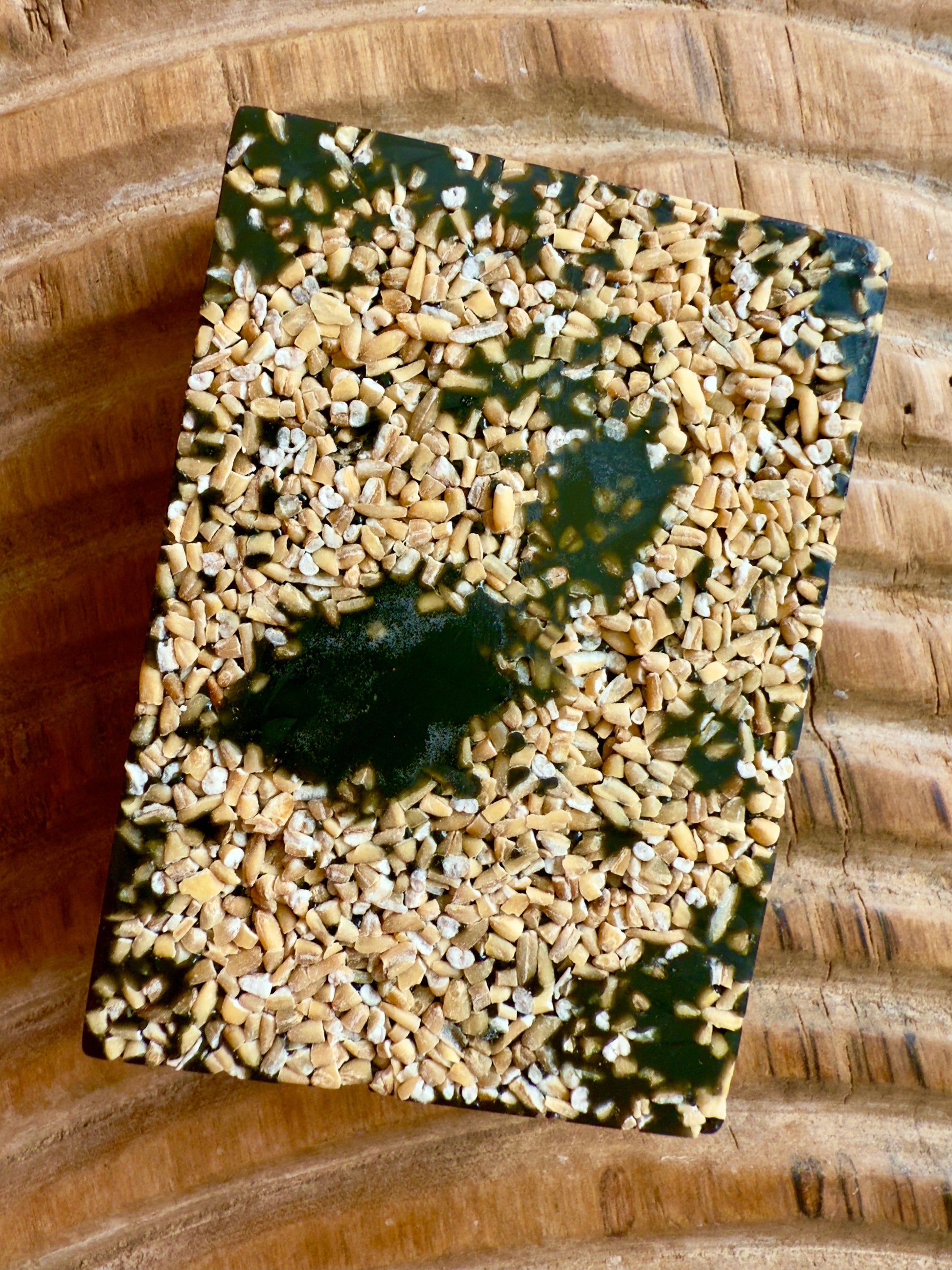 Dark African black soap bar topped with chopped oats, showing natural texture and rugged finish.