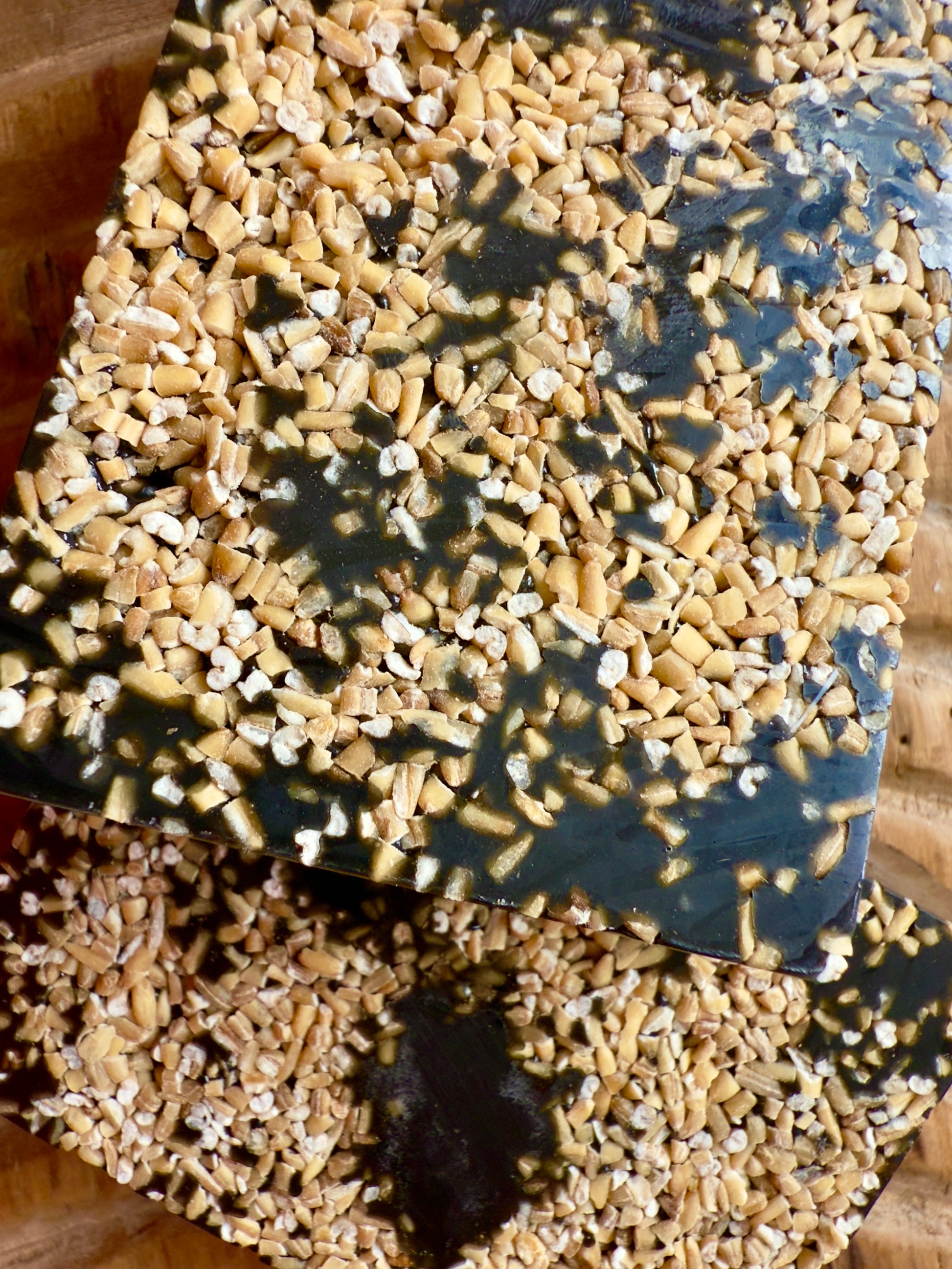 Dark African black soap bar topped with chopped oats, showing natural texture and rugged finish.