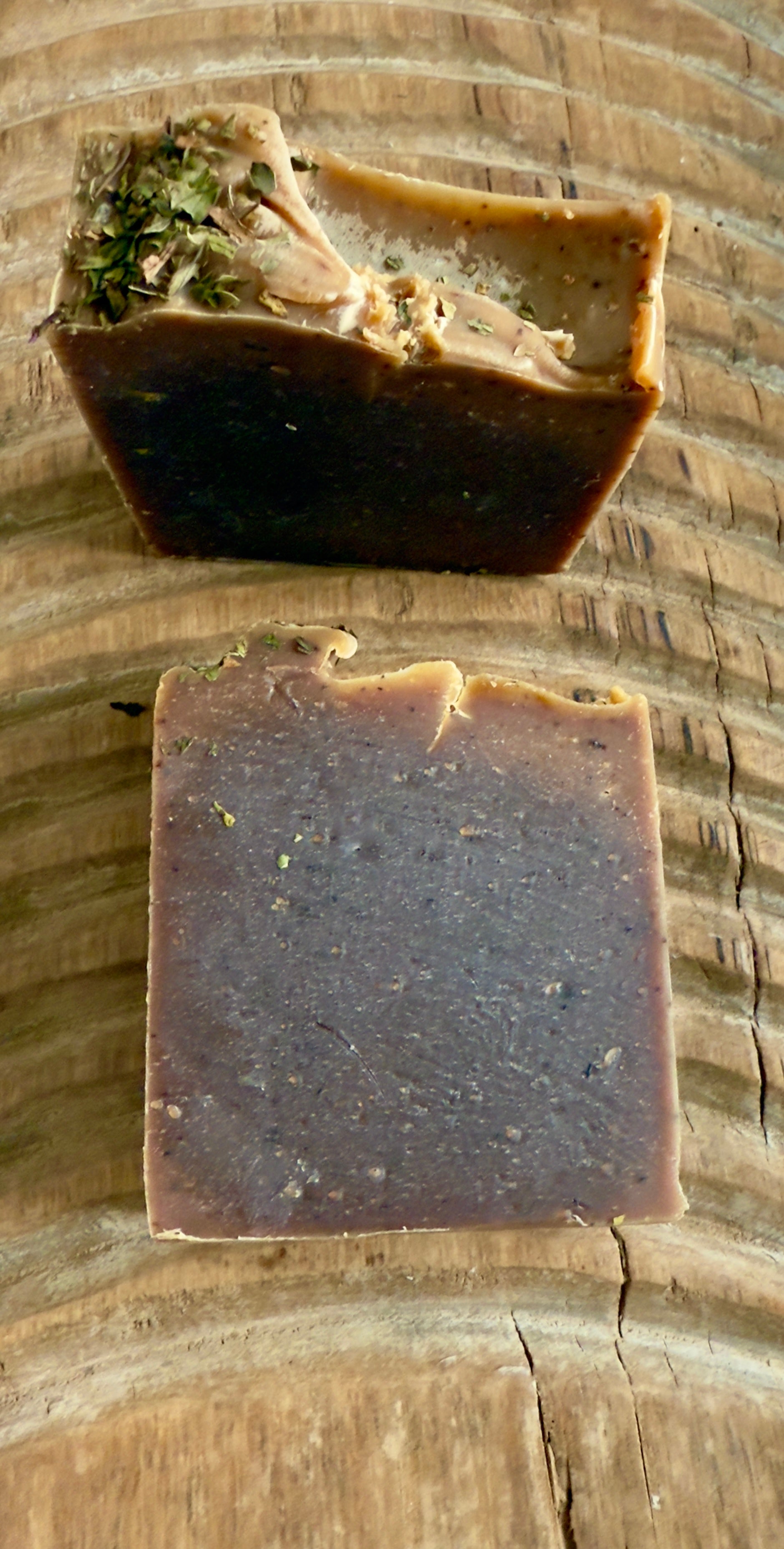 Deep brown Peppermint Cocoa cold process soap topped with crushed peppermint leaves on rustic wood.