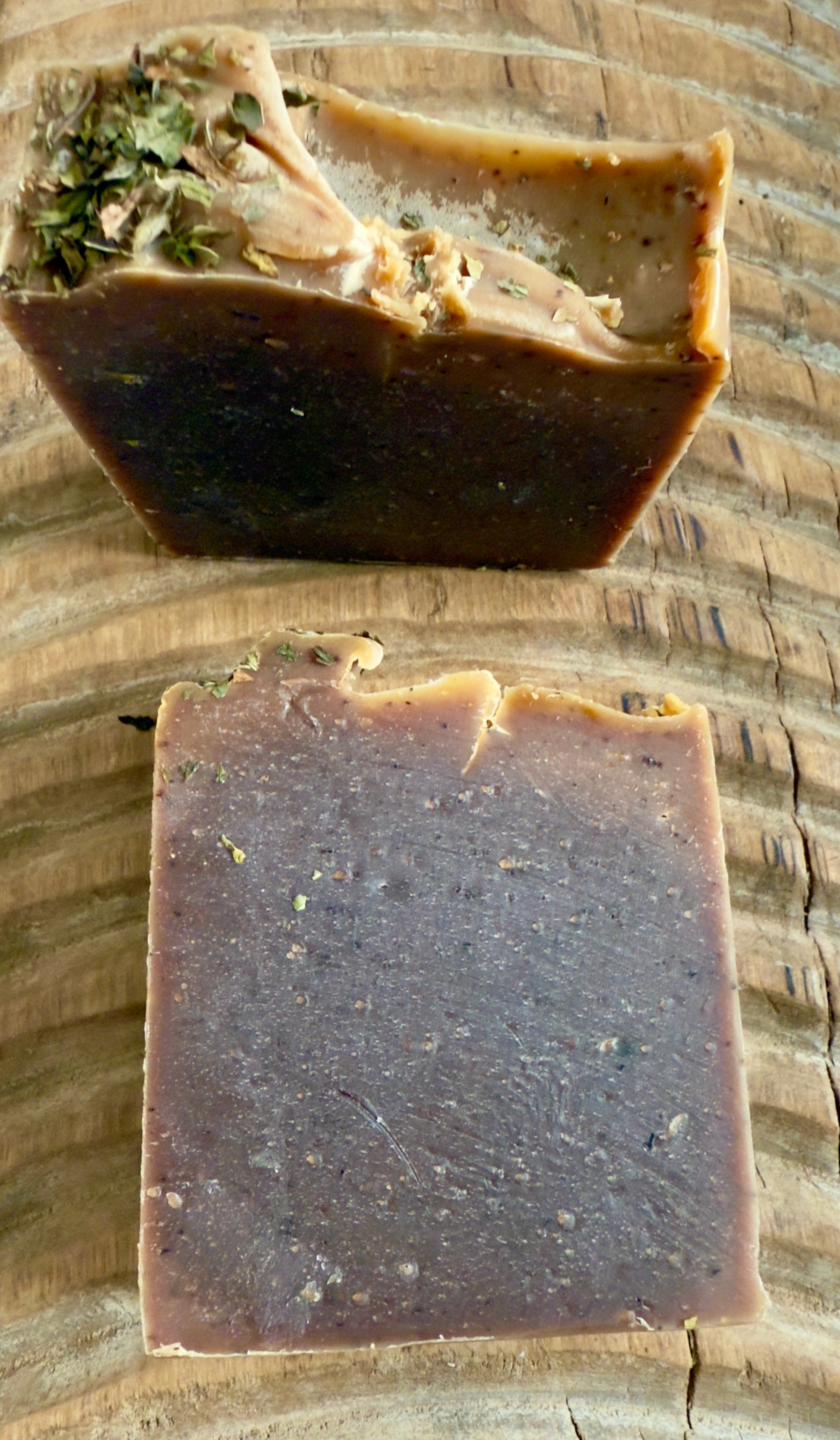 Deep brown Peppermint Cocoa cold process soap topped with crushed peppermint leaves on rustic wood.