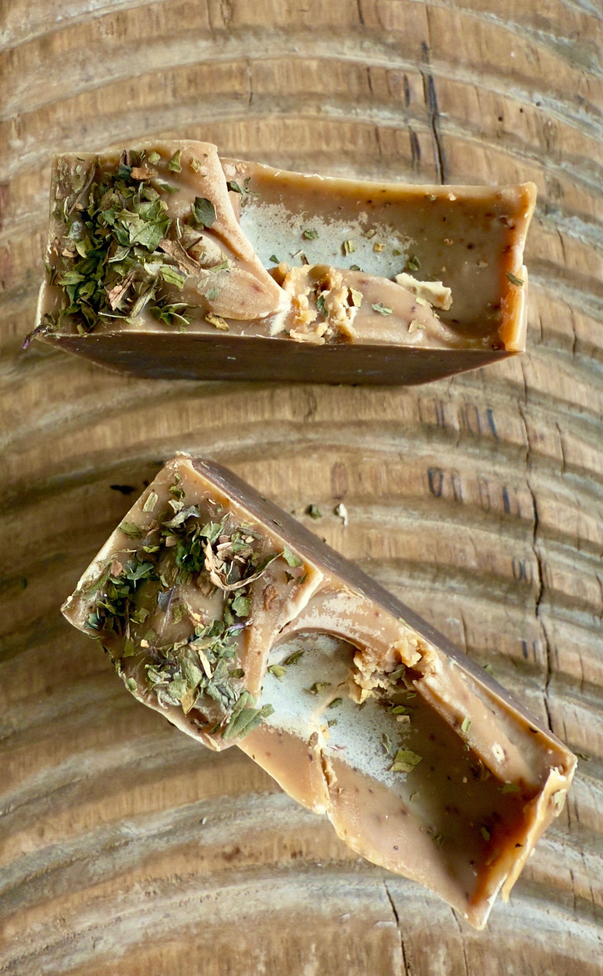 Deep brown Peppermint Cocoa cold process soap topped with crushed peppermint leaves on rustic wood.