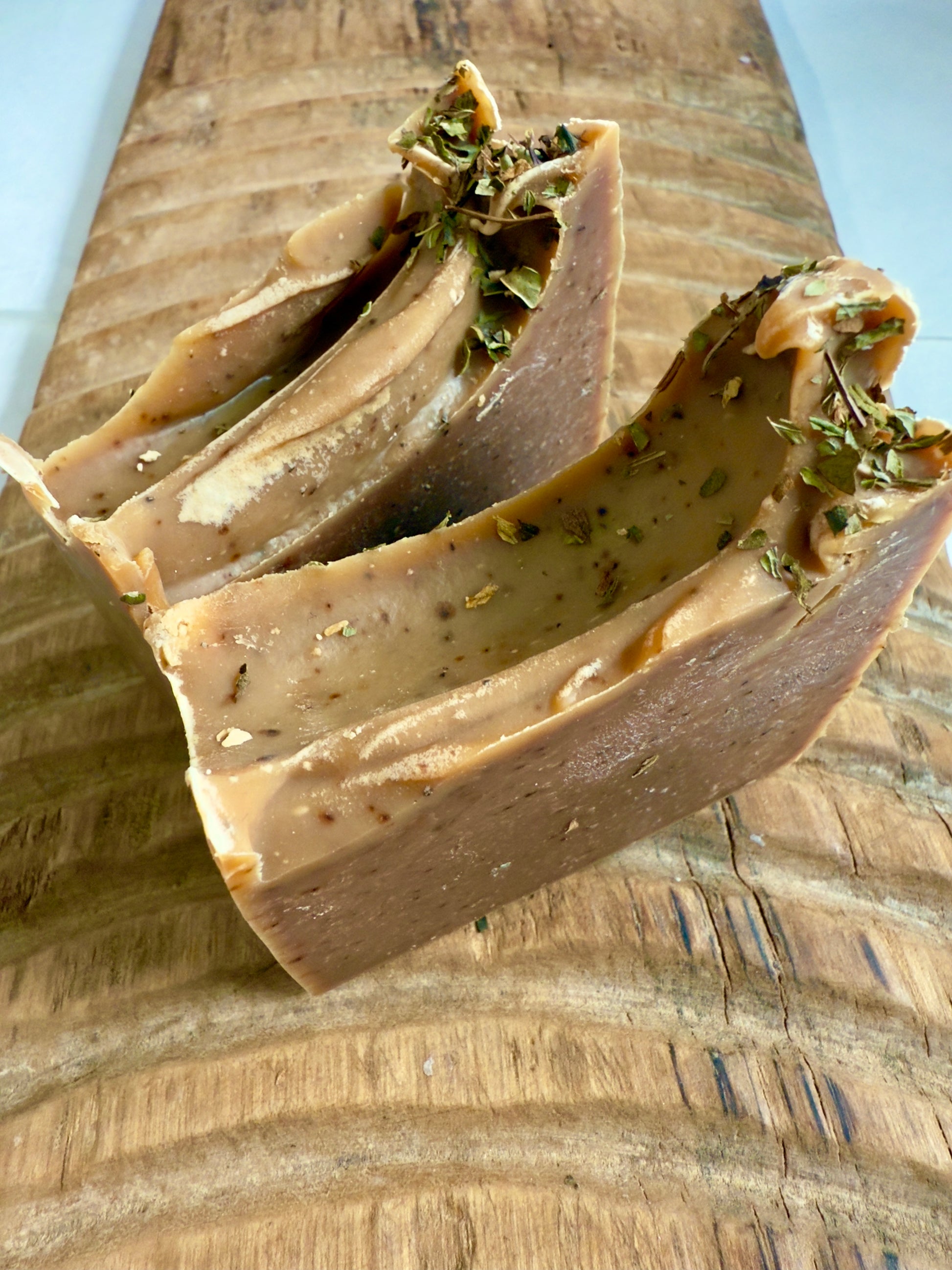 Deep brown Peppermint Cocoa cold process soap topped with crushed peppermint leaves on rustic wood.