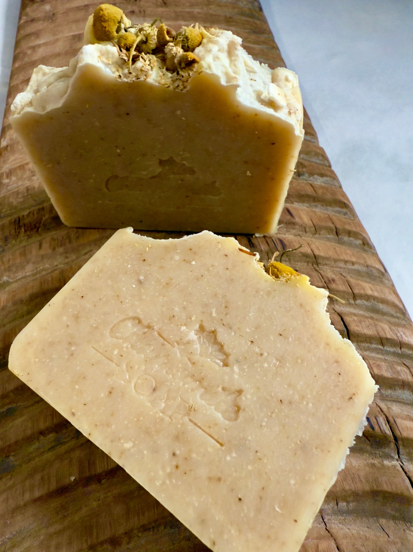 Chamomile cold process soap with a soft natural tone, speckles throughout, and whole chamomile blossoms on top.