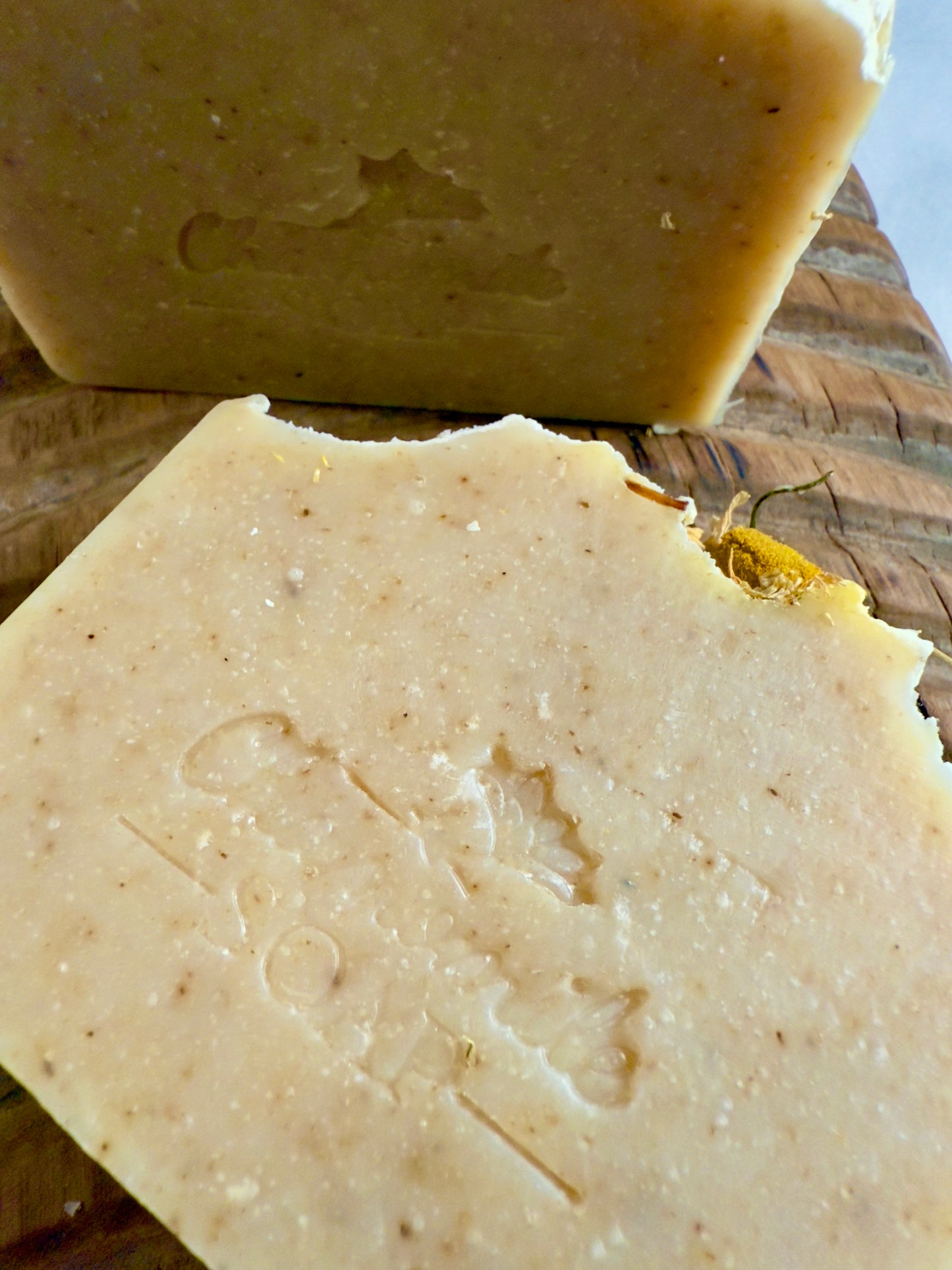 Chamomile cold process soap with a soft natural tone, speckles throughout, and whole chamomile blossoms on top.