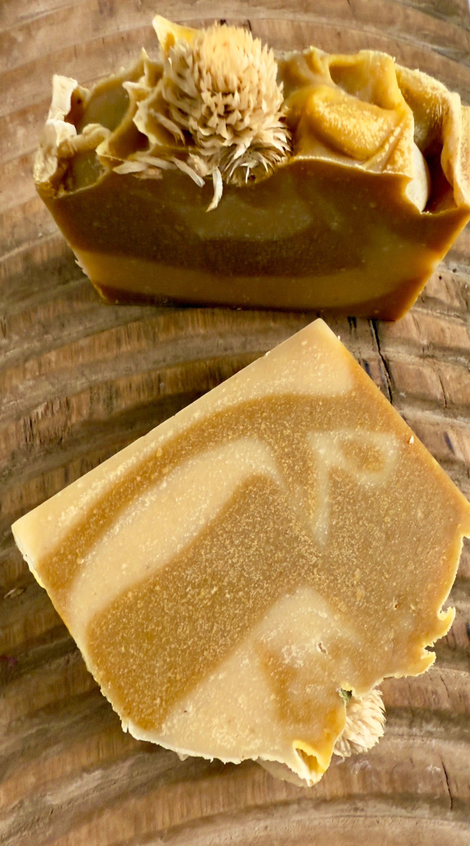 Golden swirled Autumn Harvest cold process soap topped with a dried bloom, displayed on textured wood.