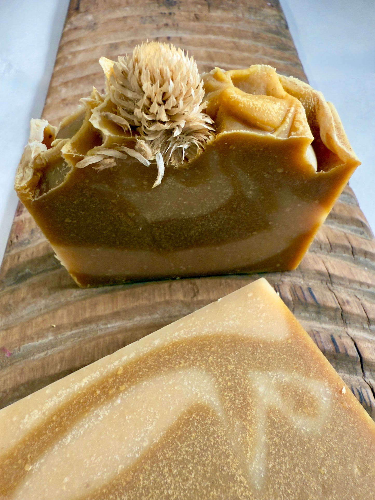 Golden swirled Autumn Harvest cold process soap topped with a dried bloom, displayed on textured wood.