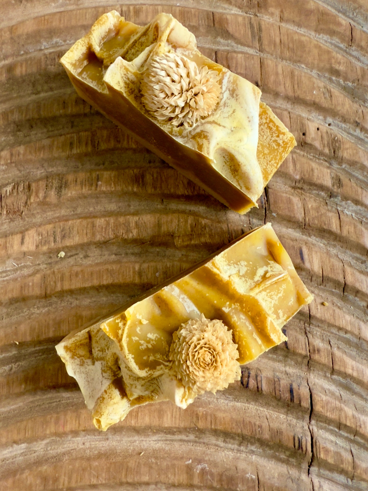 Golden swirled Autumn Harvest cold process soap topped with a dried bloom, displayed on textured wood.