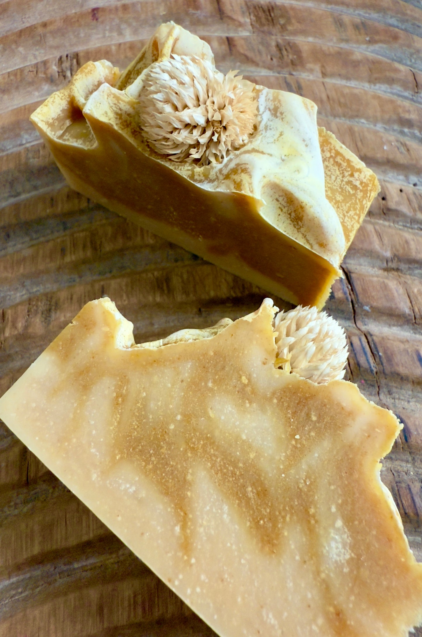 Golden swirled Autumn Harvest cold process soap topped with a dried bloom, displayed on textured wood.