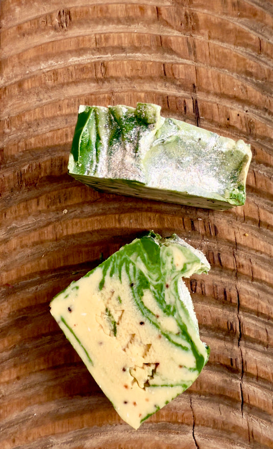 Green and cream marbled soap bars with light cranberry seed speckles on a carved wooden board.