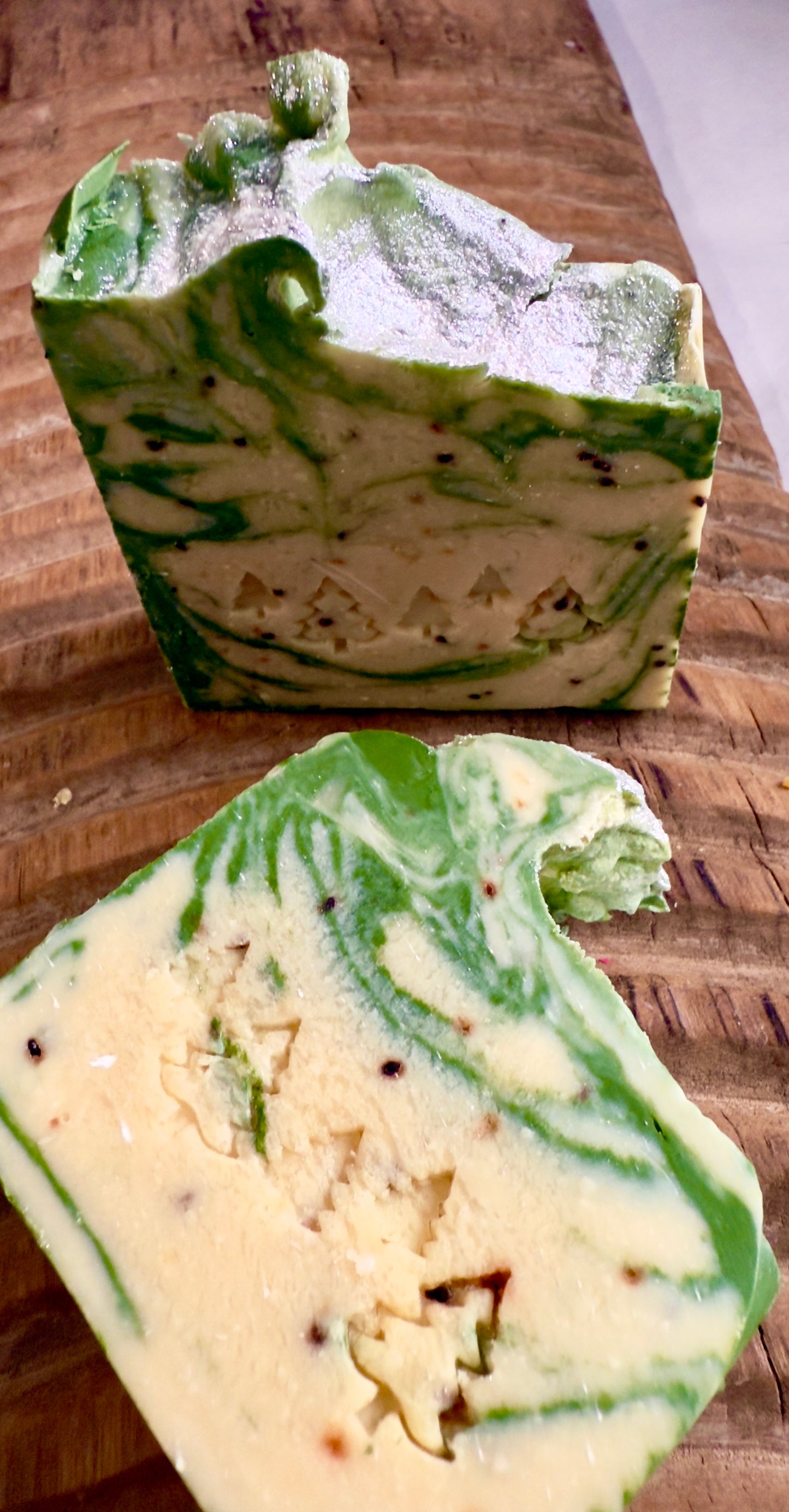 Green and cream marbled soap bars with light cranberry seed speckles on a carved wooden board.
