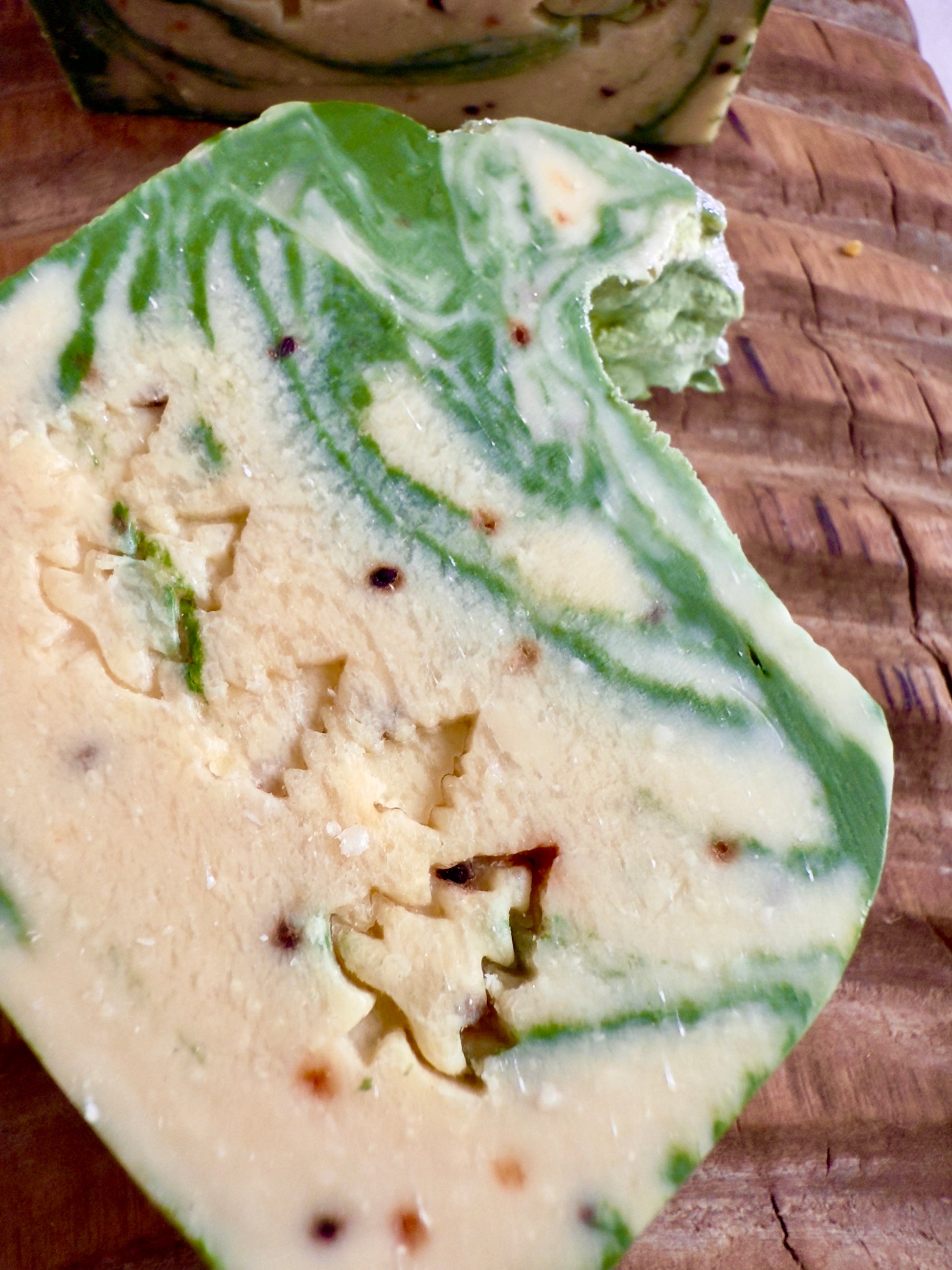 Green and cream marbled soap bars with light cranberry seed speckles on a carved wooden board.