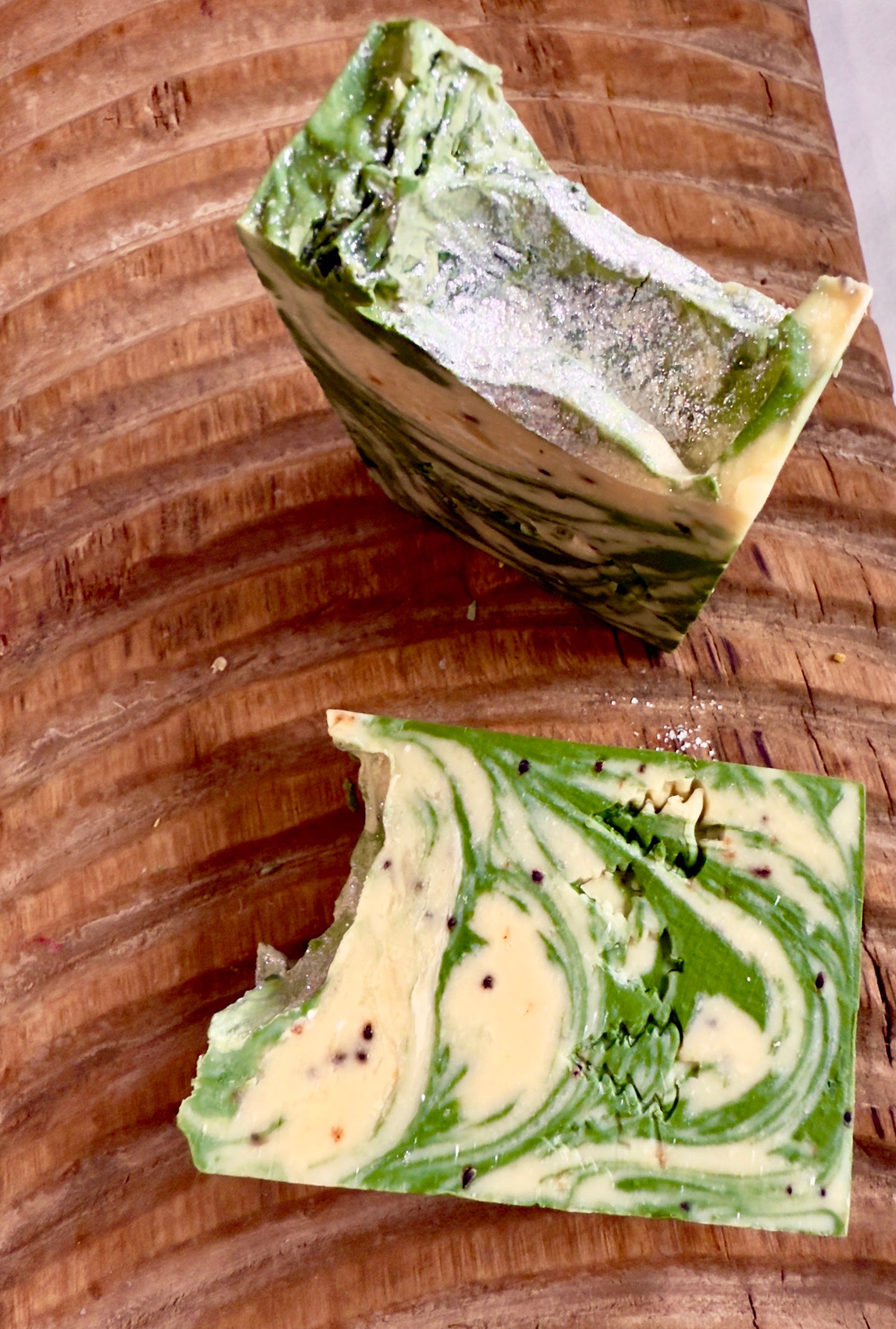 Green and cream marbled soap bars with light cranberry seed speckles on a carved wooden board.