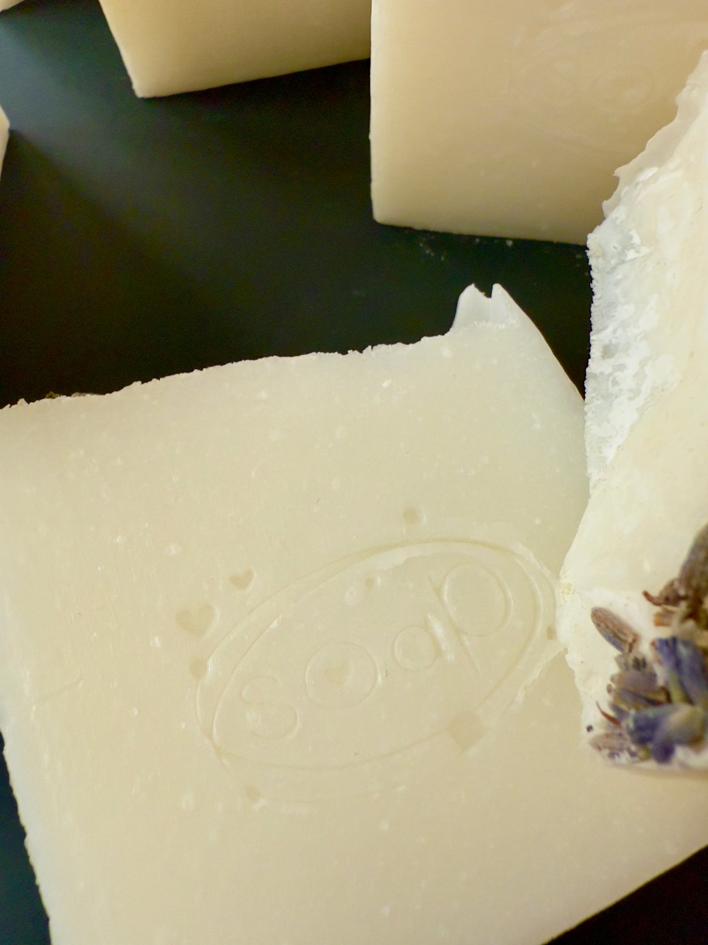 Creamy white tallow soap bars with lavender buds on top, arranged against a dark background.