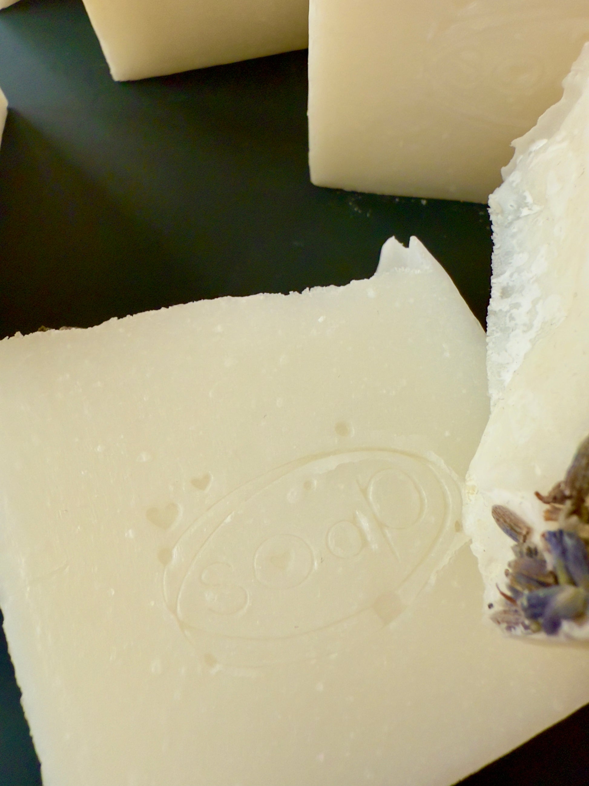 Creamy white tallow soap bars with lavender buds on top, arranged against a dark background.