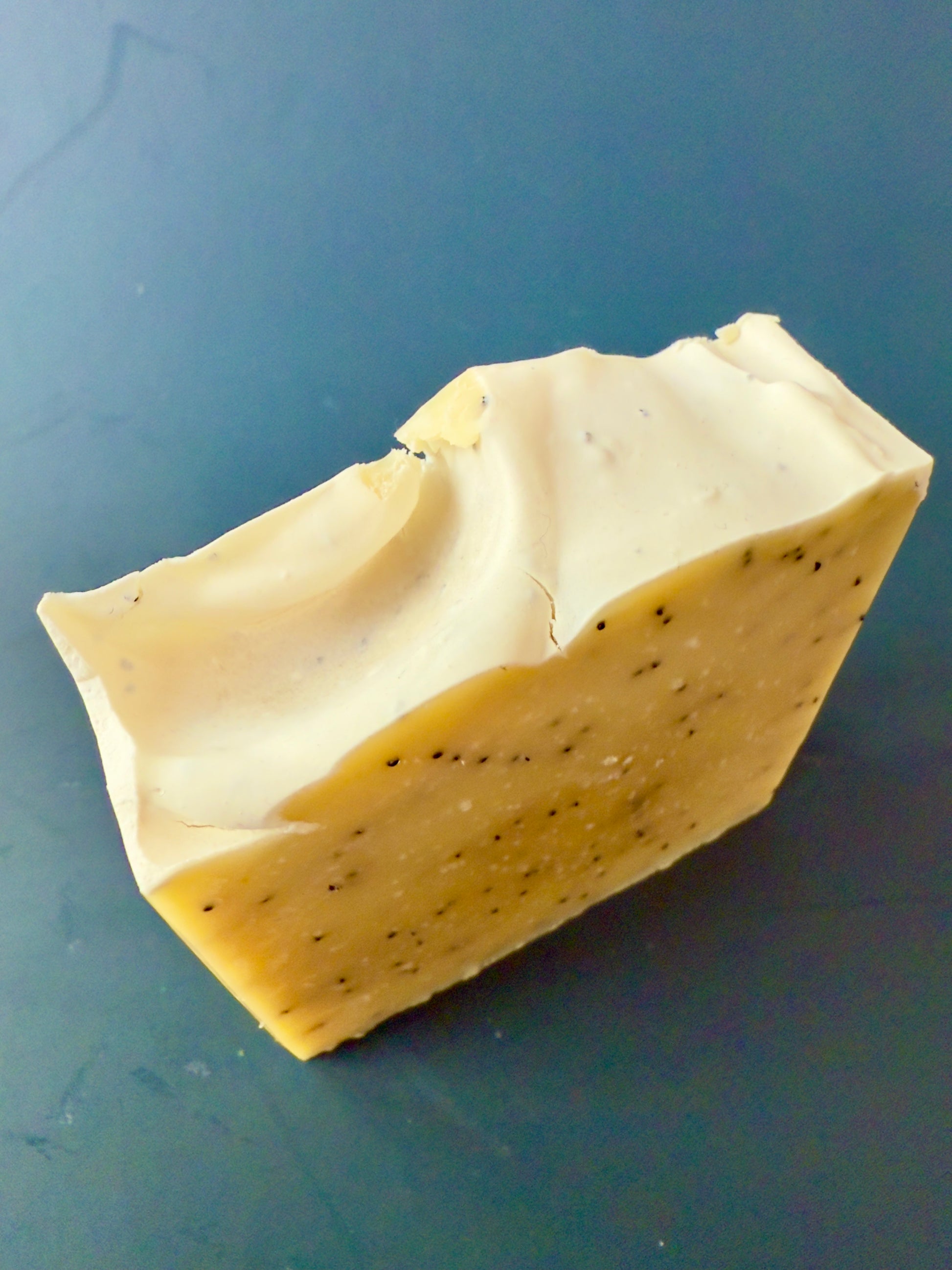 Lemon-colored soap bar with poppy seeds, displayed on a dark teal background.